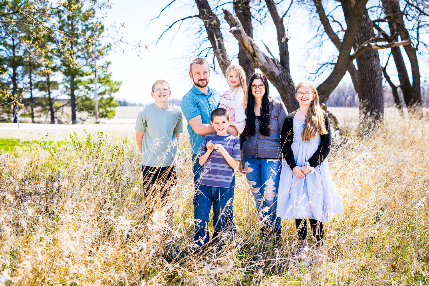 Family enjoying a playful moment together in a grassy field during golden hour sunset.