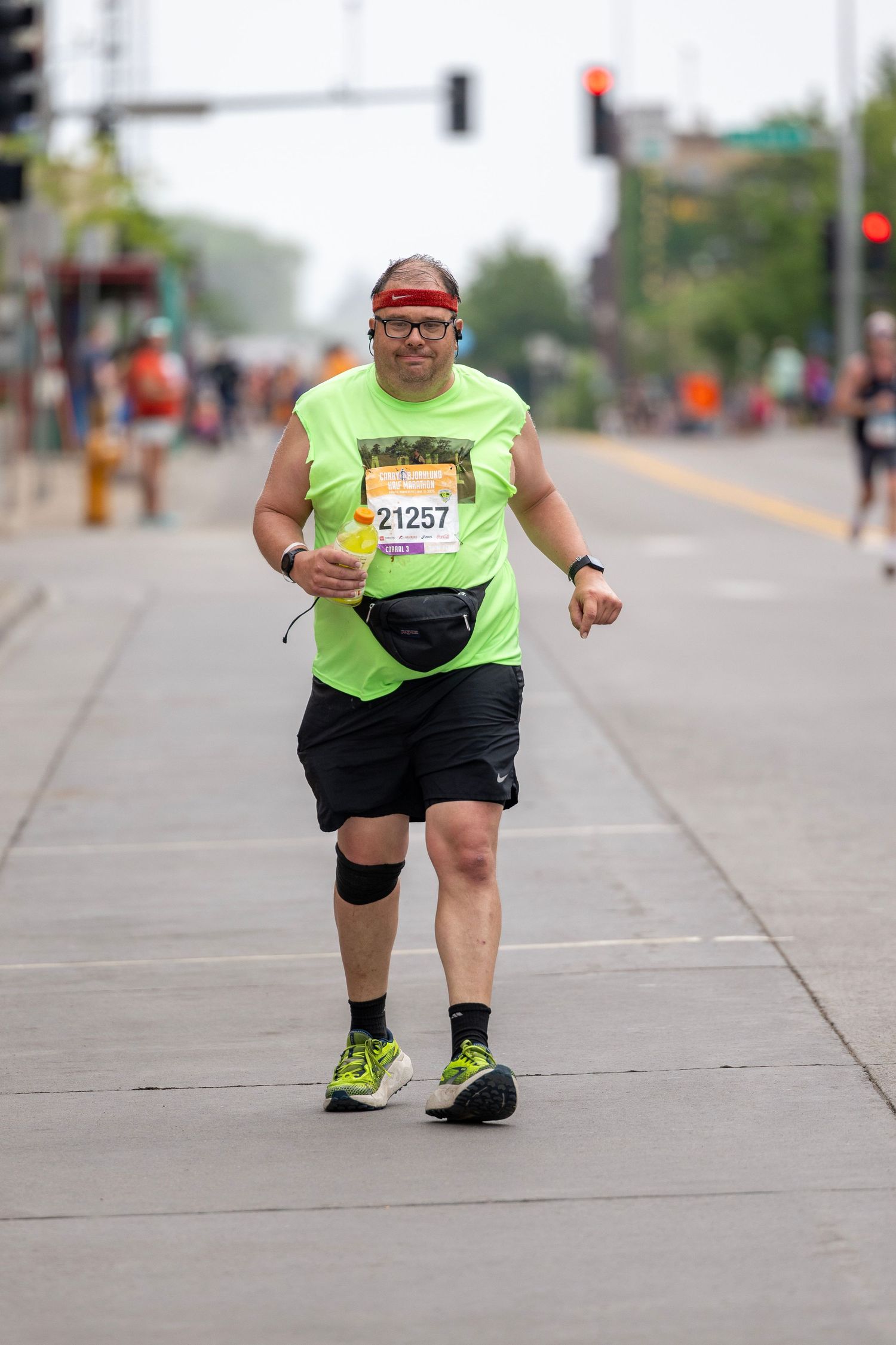 Runner in bright yellow shirt and black shorts moving along city sidewalk during race.