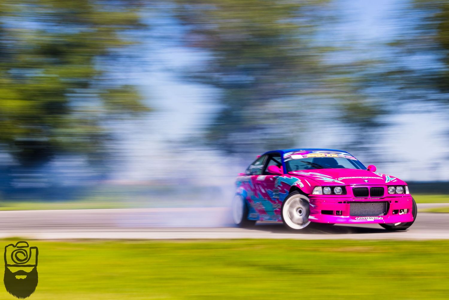Pink modified race car speeds past on track with dramatic motion blur.