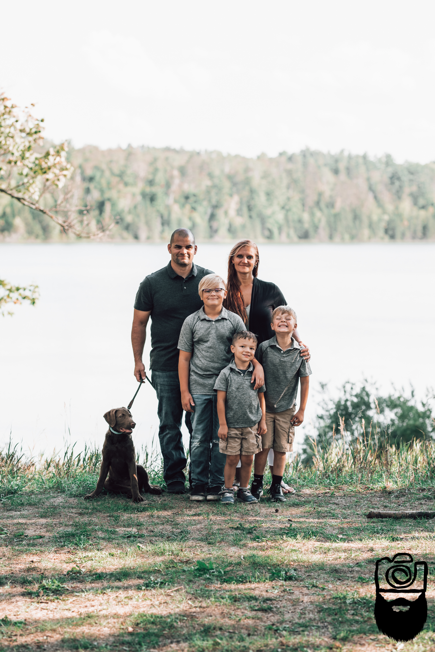 Family with children and dog posing together by scenic lake.