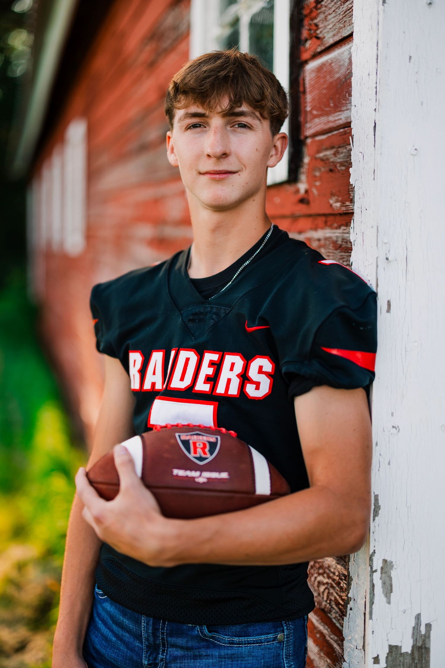 A Raiders football jersey is worn while posing against a red brick wall.