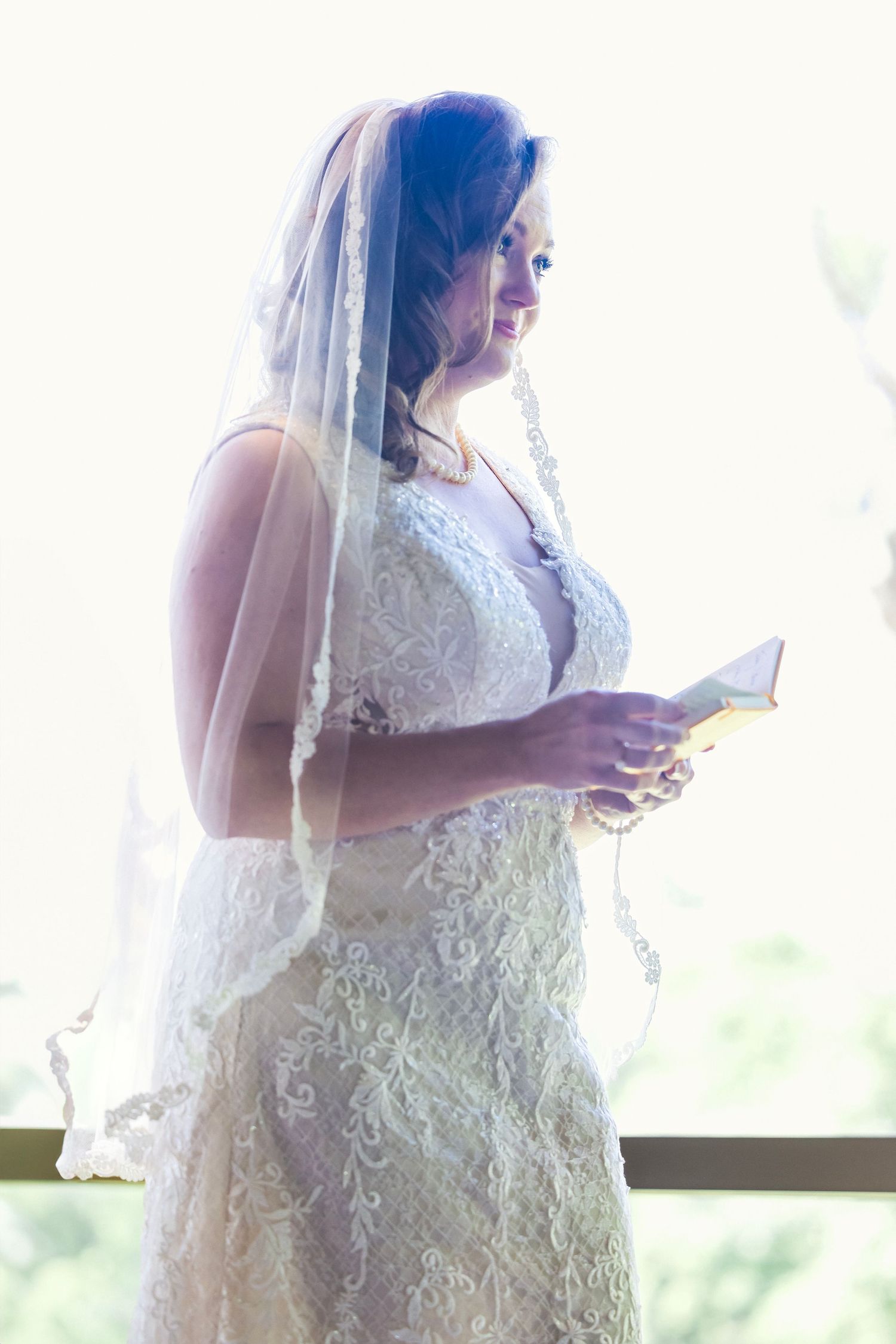 Ethereal bridal portrait showing lace dress details and flowing veil in natural light.