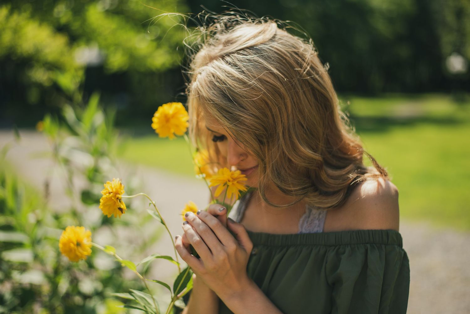 Person in green dress near blooming yellow daffodils in a garden.
