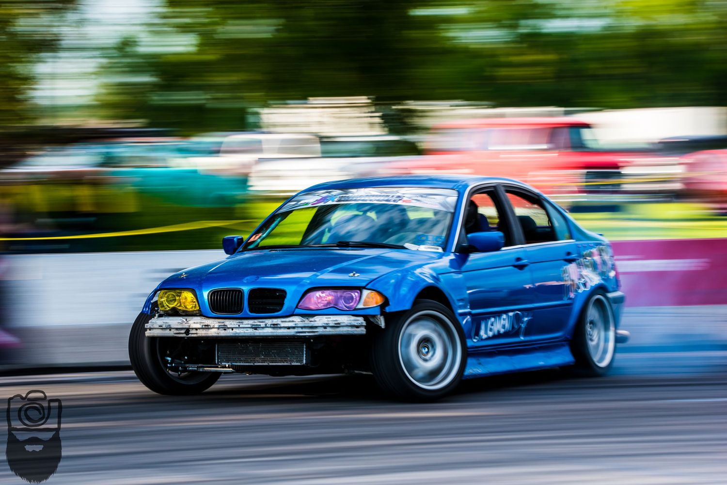 Motion-blurred BMW vehicles racing on a track with colorful paint schemes.
