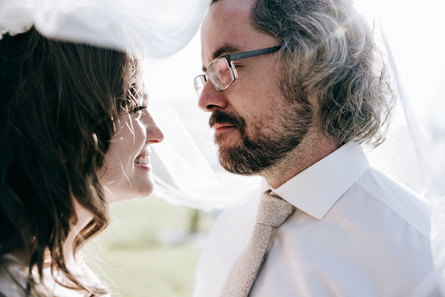 Close-up profile view of couple in wedding attire gazing at each other with tender expressions.