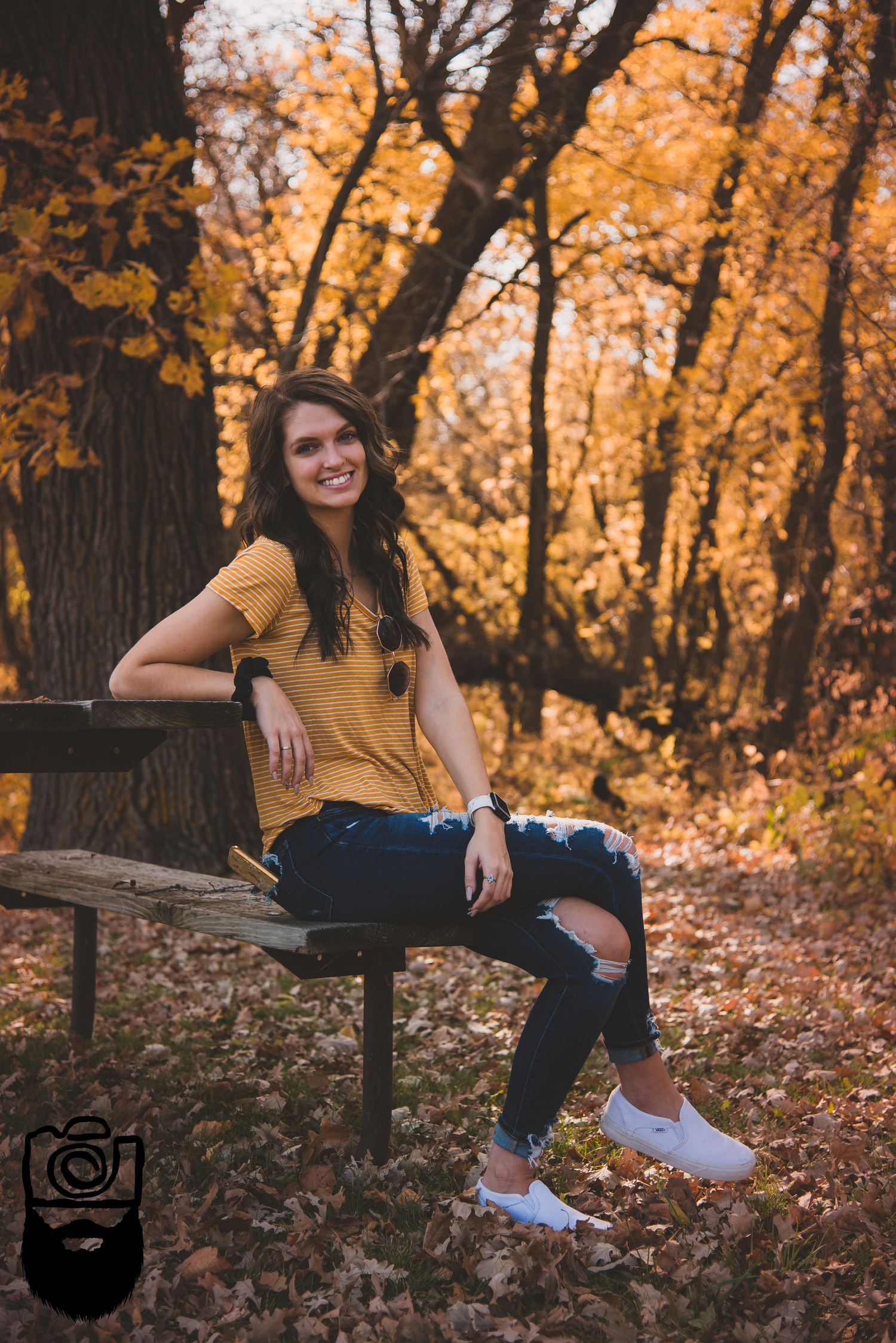 Person in mustard top sitting on park bench surrounded by golden fall foliage.