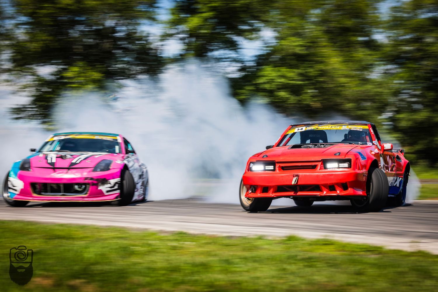 Colorful drift cars creating smoke while competing on a professional racing track.