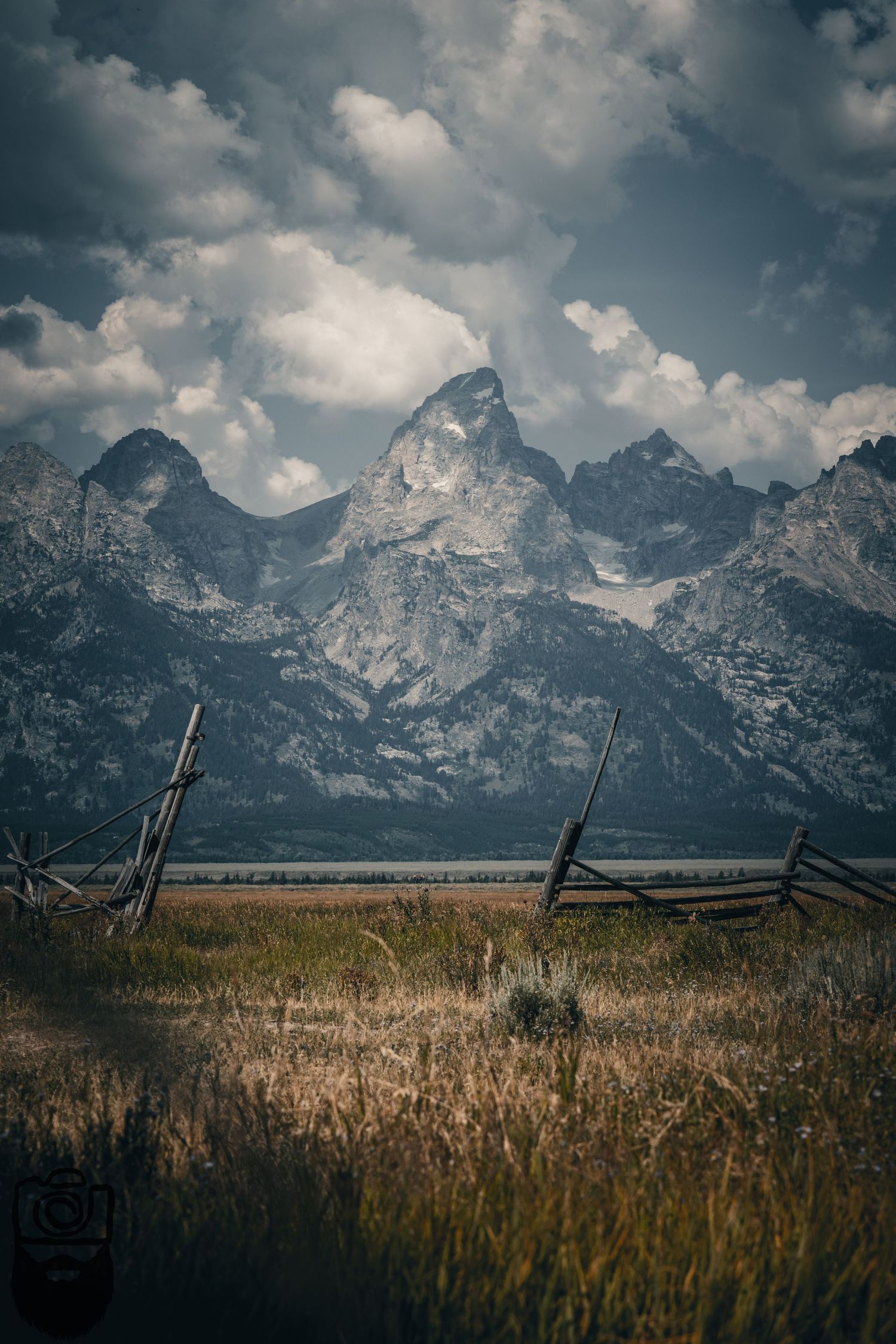 Split-rail fence runs along prairie grass with Teton mountains in background.