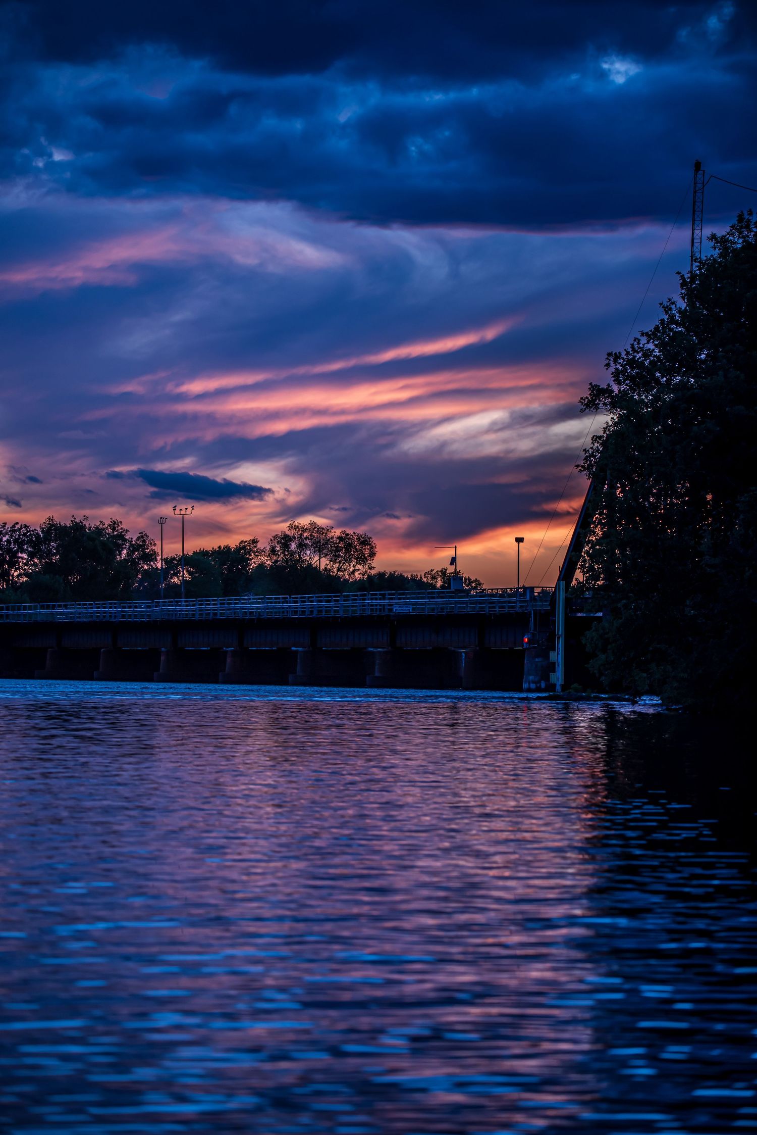 Dramatic purple and pink sunset over calm water with silhouetted trees in the background.