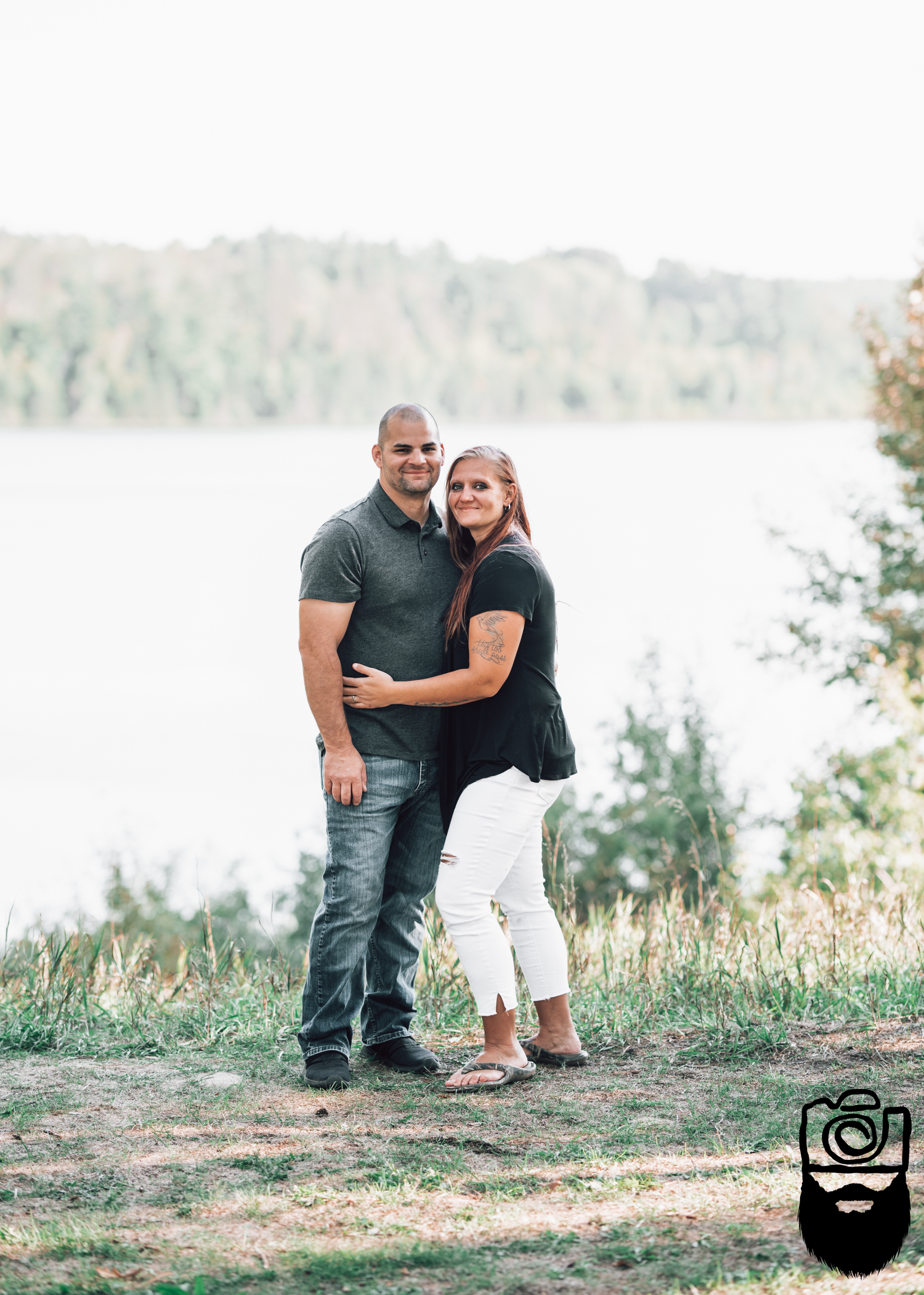 Couple embracing on hillside with lake view in background.