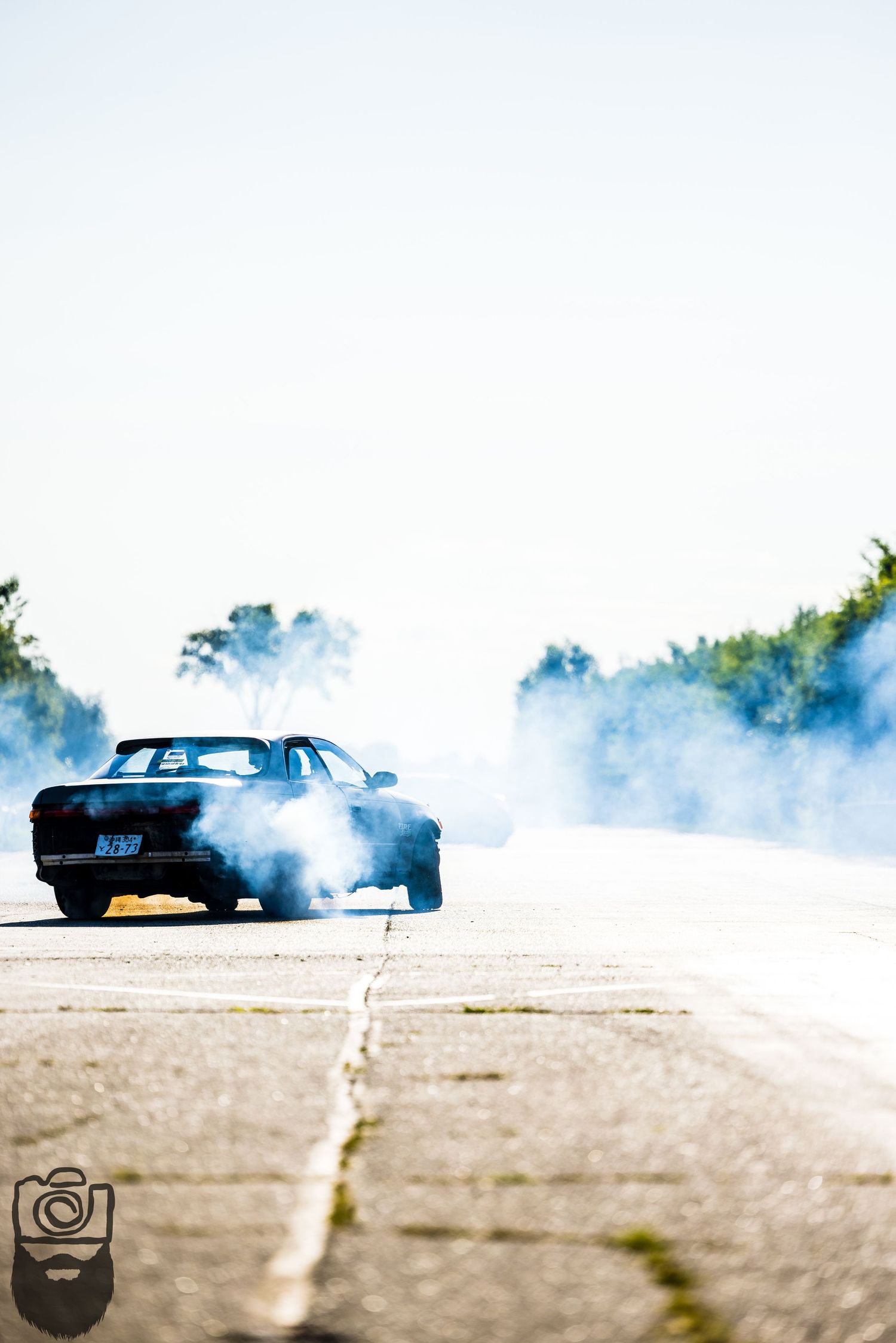 Blue car performing a burnout on pavement creating dramatic smoke effects.
