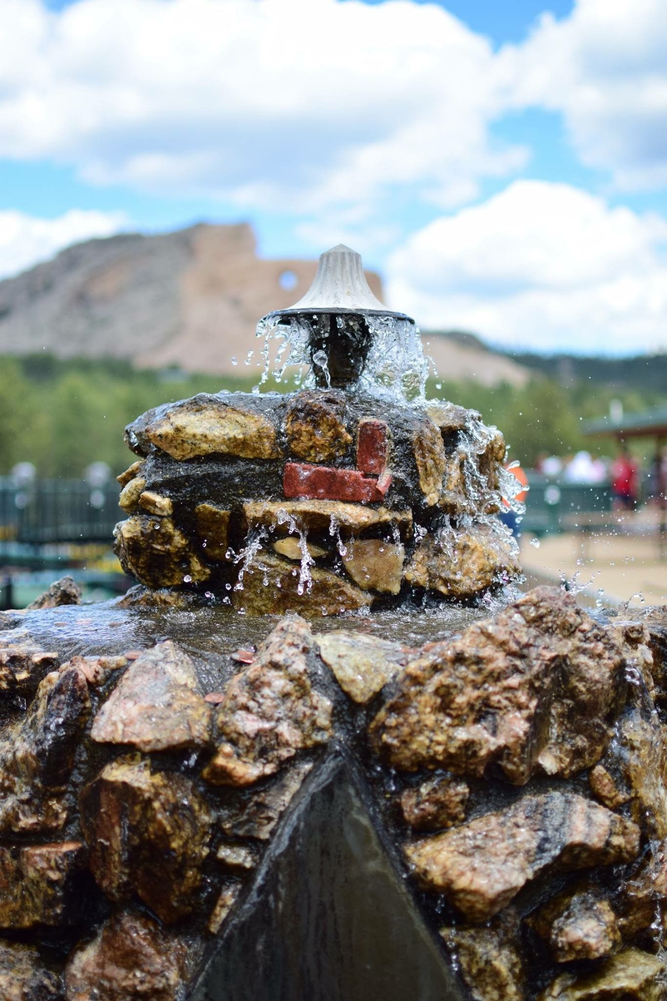Water fountain spraying over rocky formations with mountains in the background.