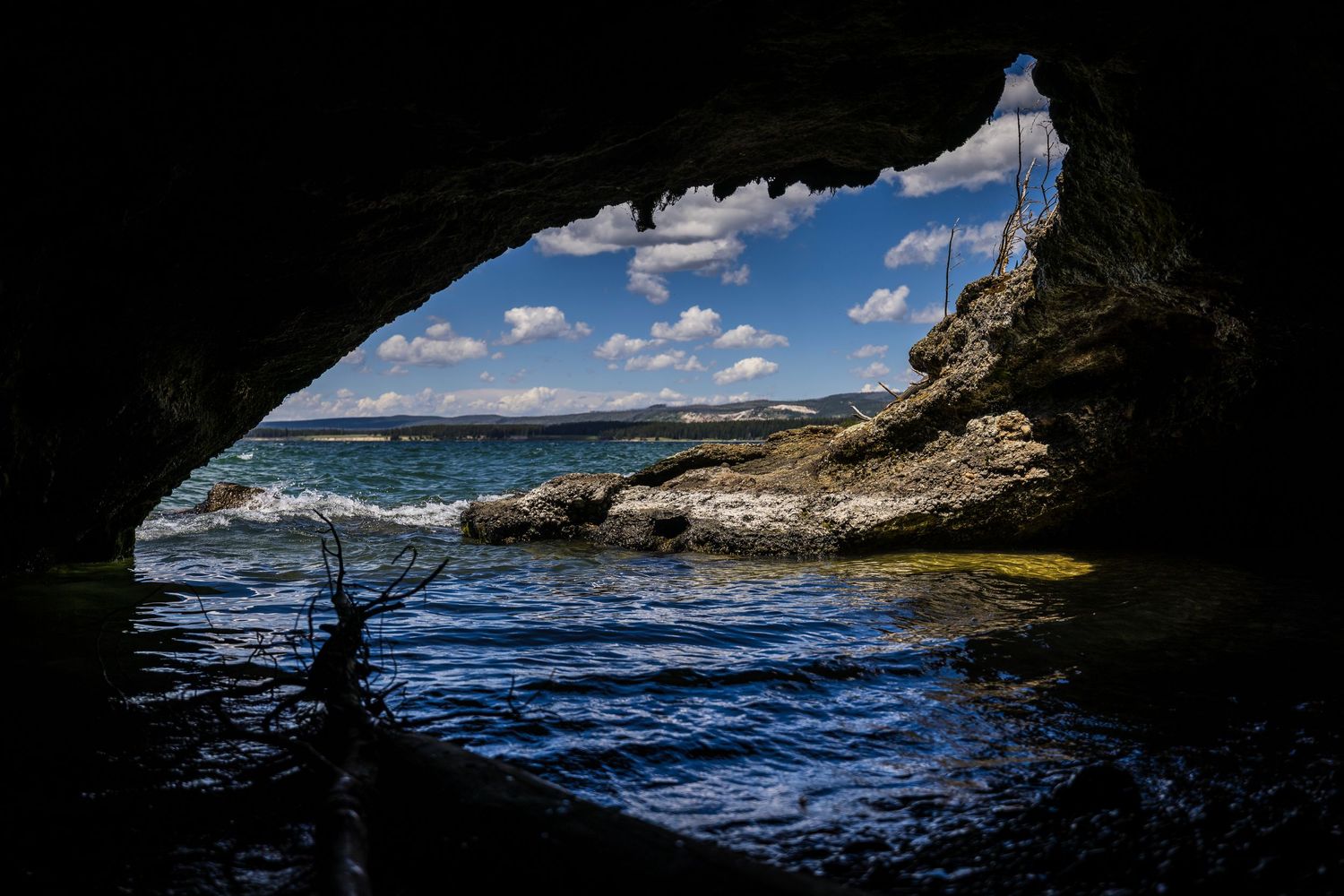 Panoramic view from inside a sea cave looking out towards blue ocean waters and rocky cliffs.