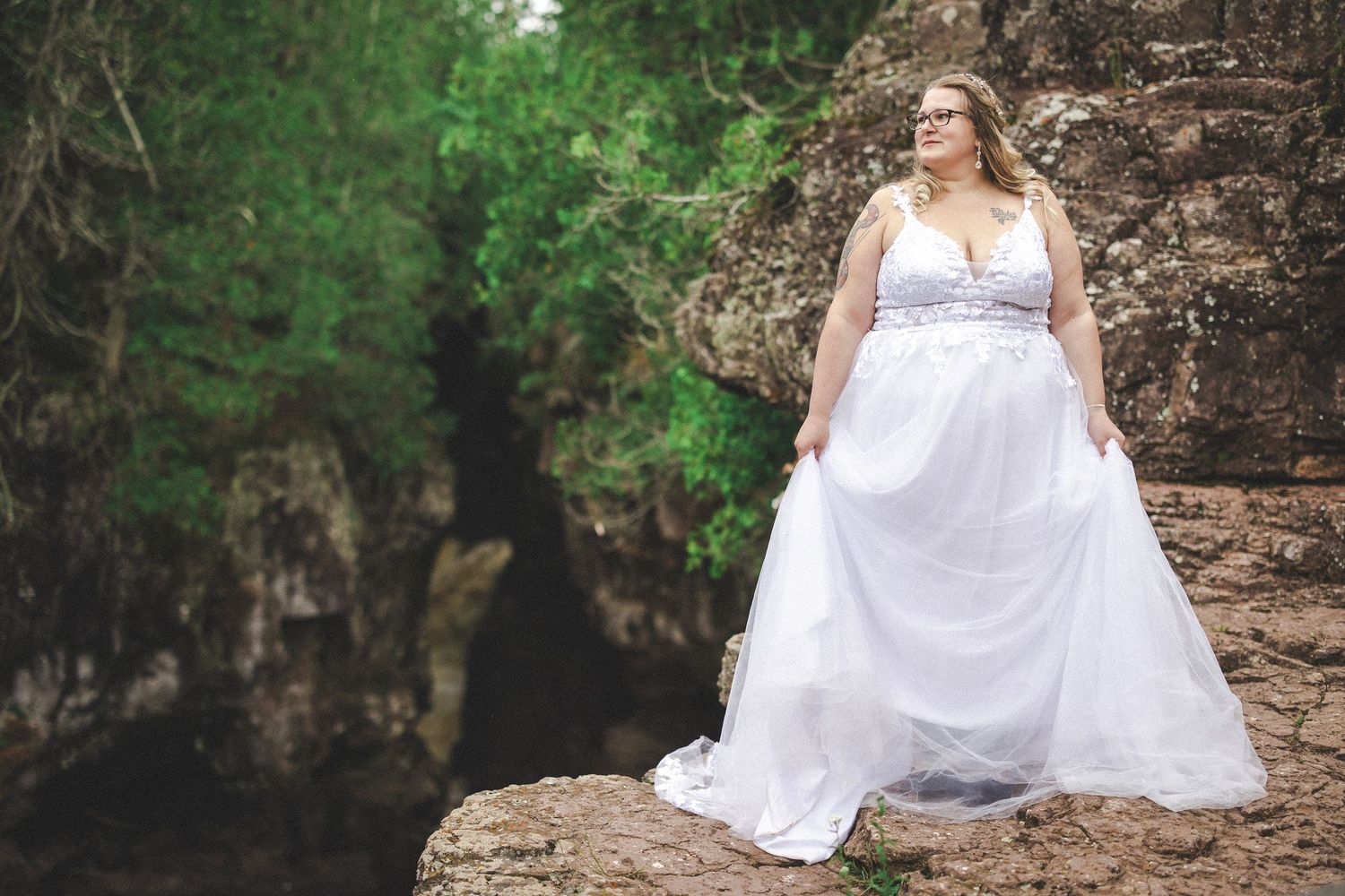 A wedding couple poses against a natural rock formation in a forest setting.