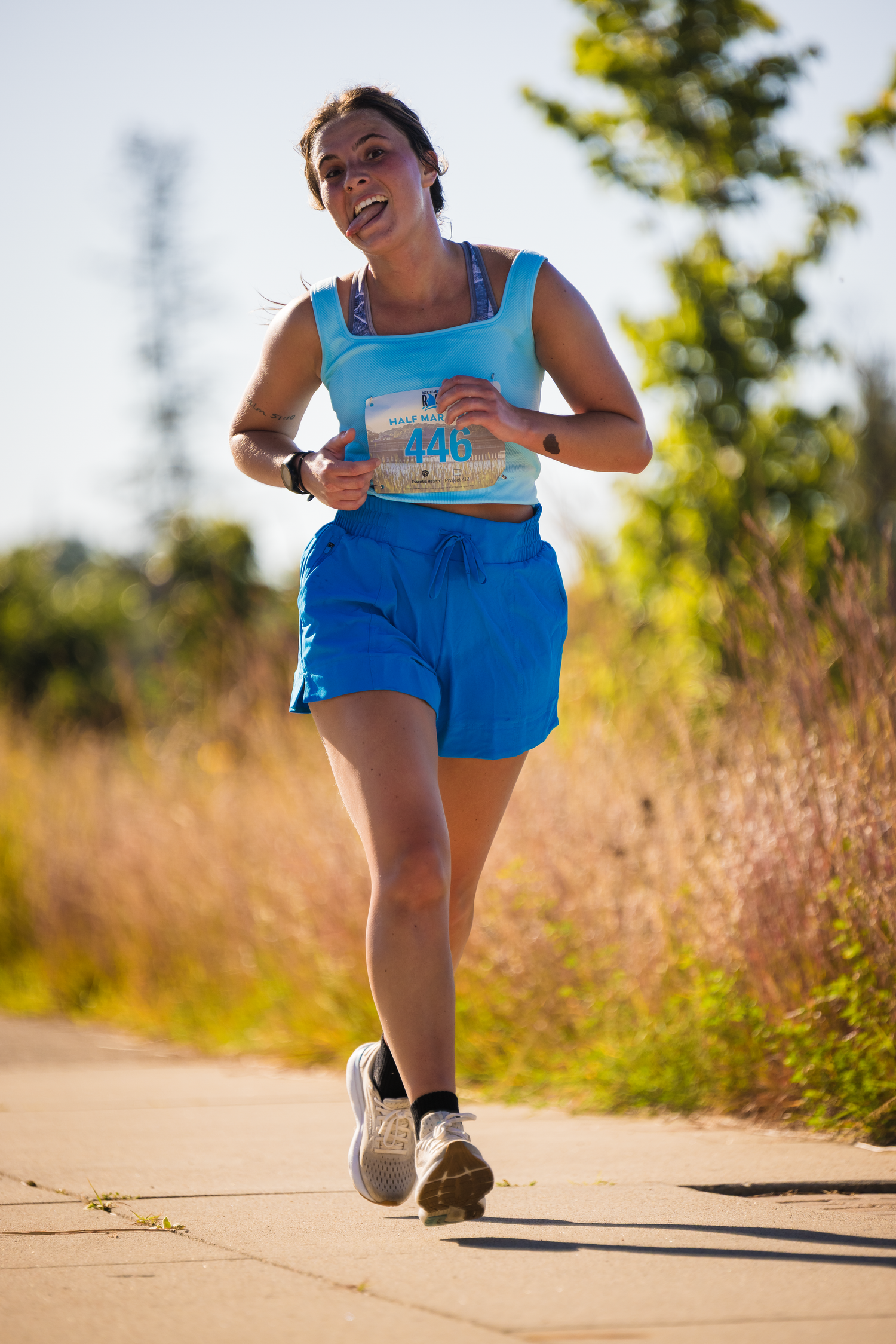 Runner in bright blue athletic wear moves along a dirt path during a sunny race event.