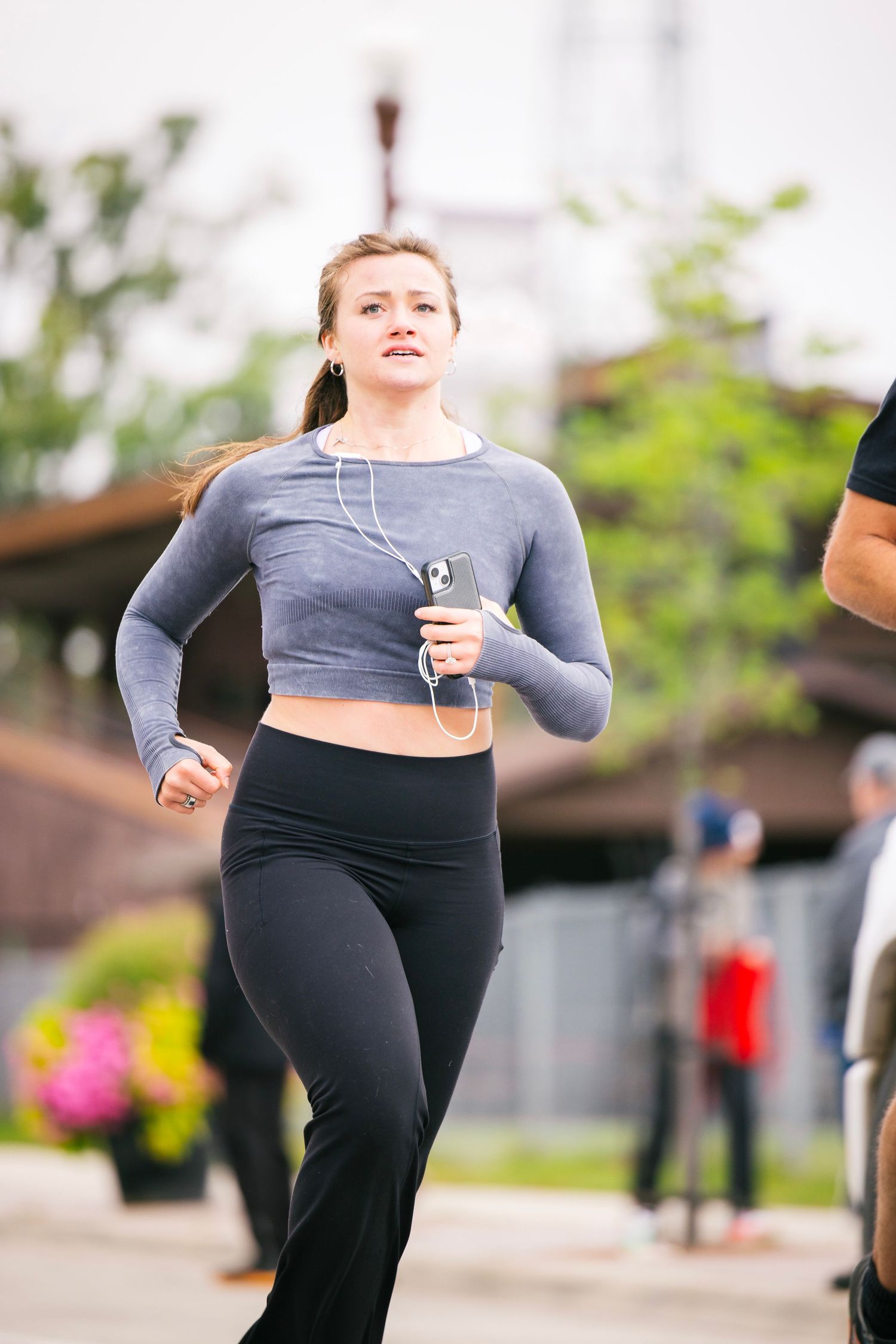 Runner in grey crop top and black leggings sprints during outdoor race competition.