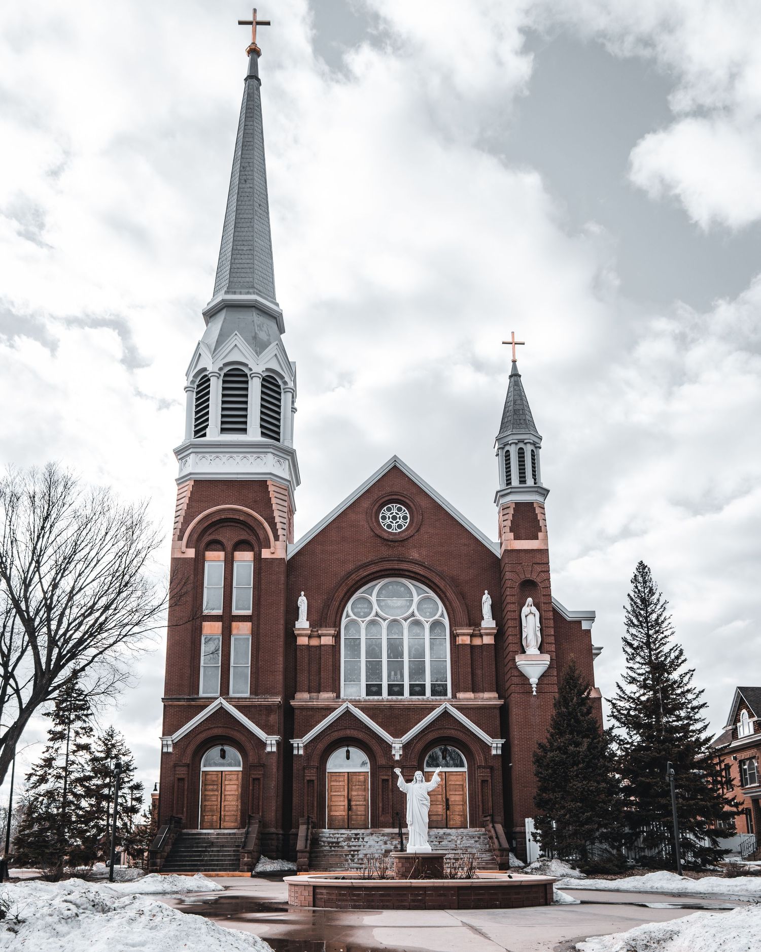 Red brick Gothic church with white spires and steeples surrounded by snow.