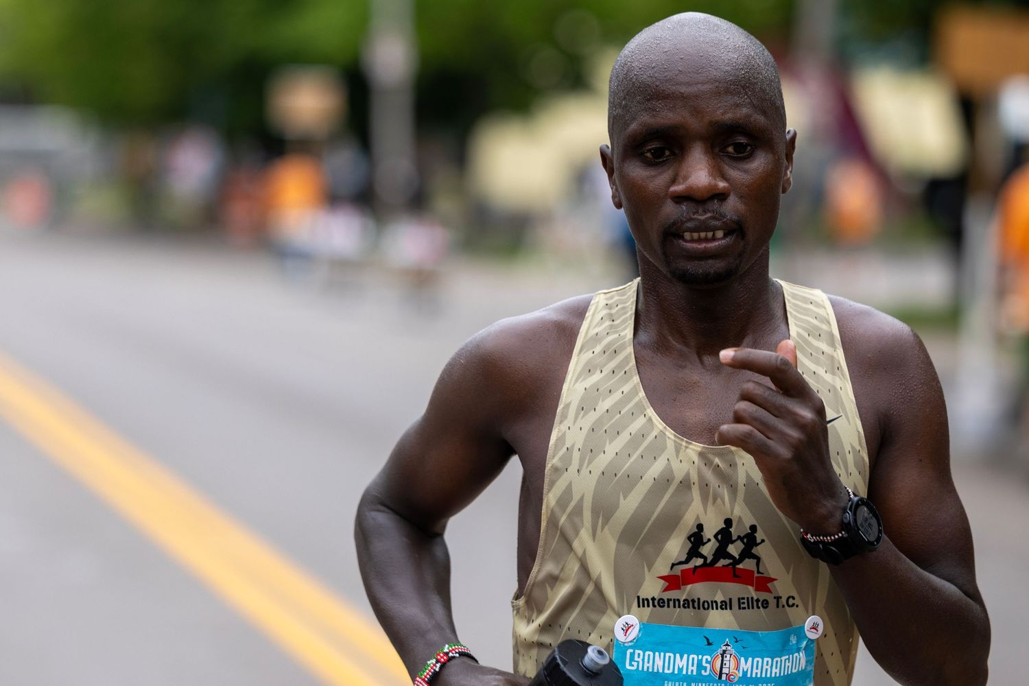 Marathon participant in tank top and shorts running along urban race course.