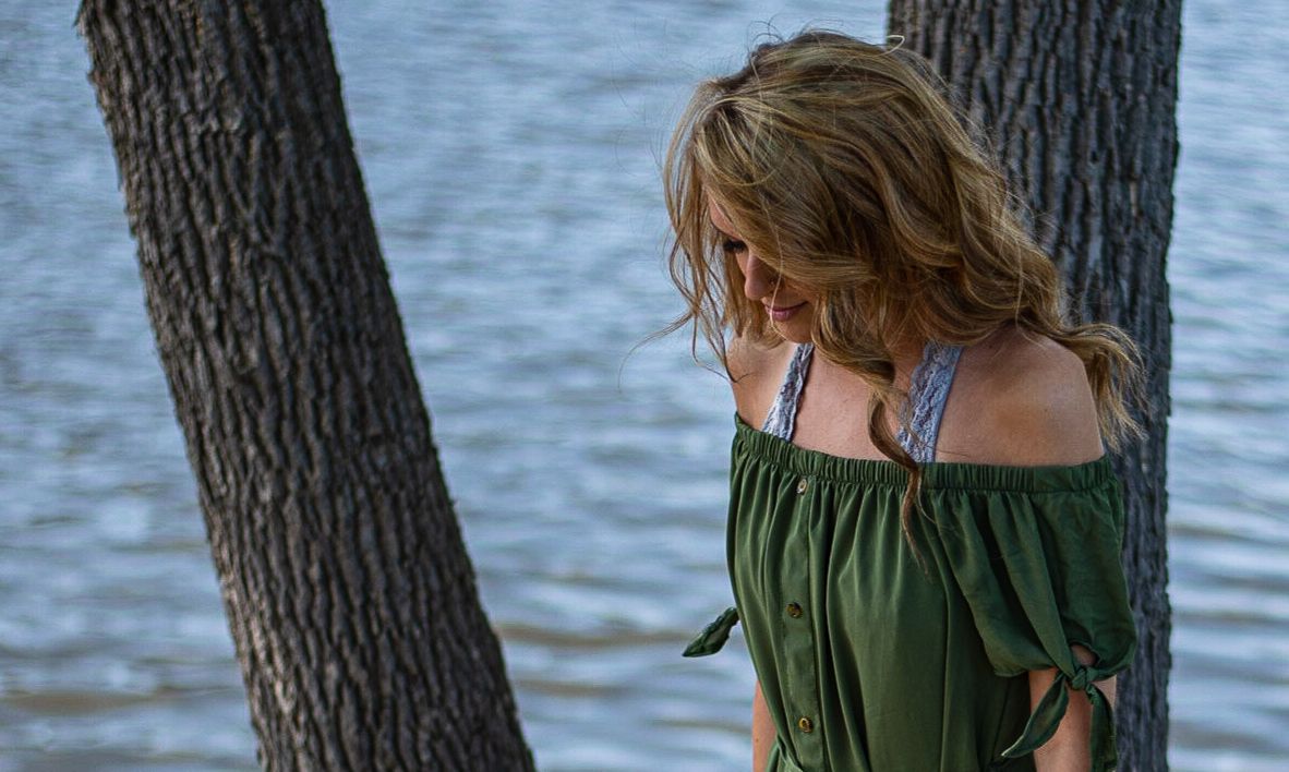 Person in a green dress sitting near water on a sunny day.