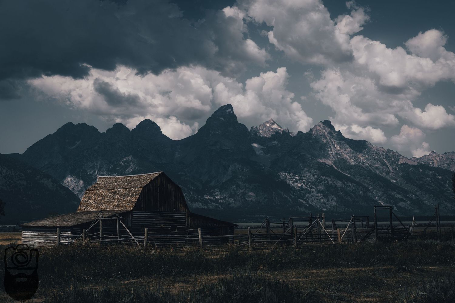 Old barn and wooden structures beneath dramatic mountain landscape.
