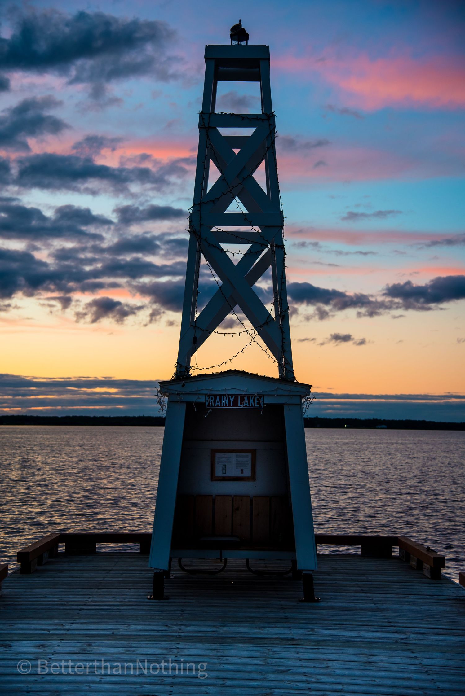Wooden pier with lookout tower silhouetted against vibrant sunset sky over ocean waters.