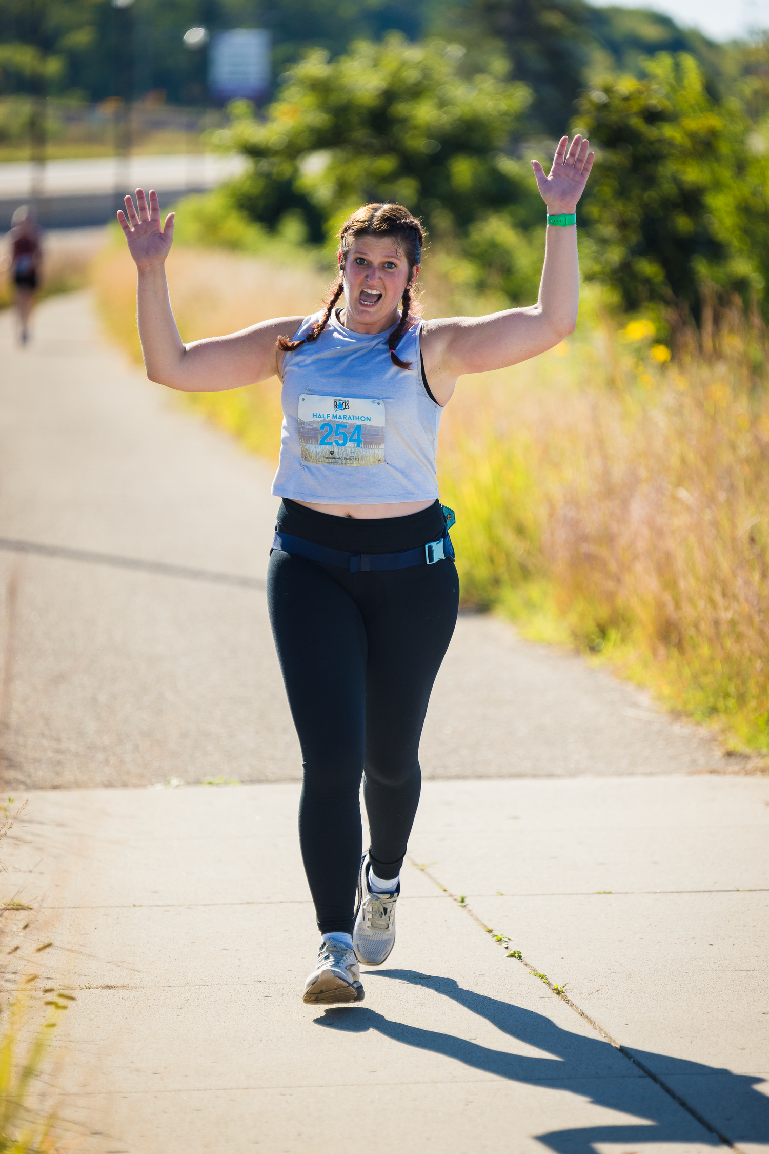 Runner in athletic wear exercising on a sunny path with arms raised triumphantly.