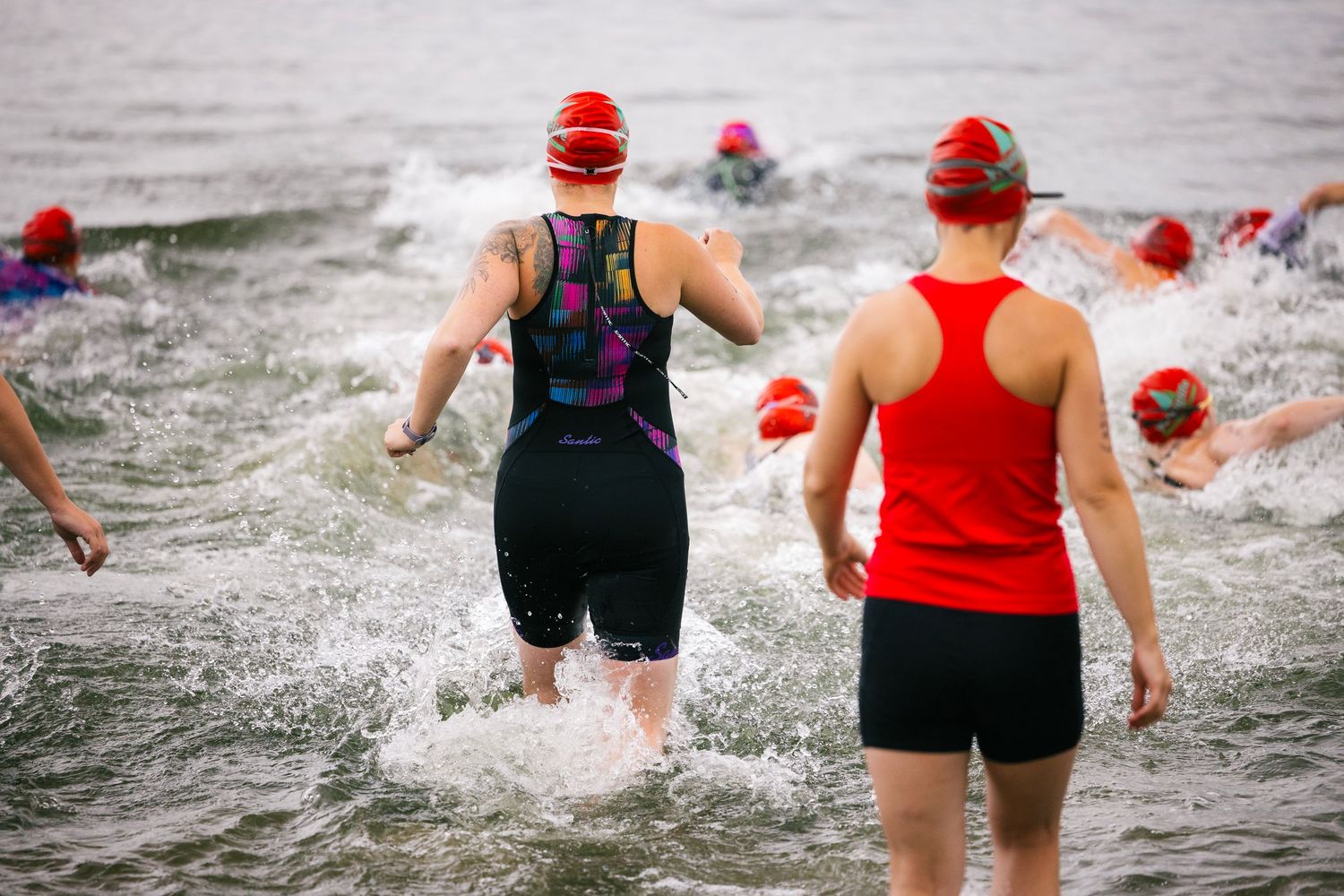 Swimmers entering the water at the start of a triathlon race wearing red swim caps.