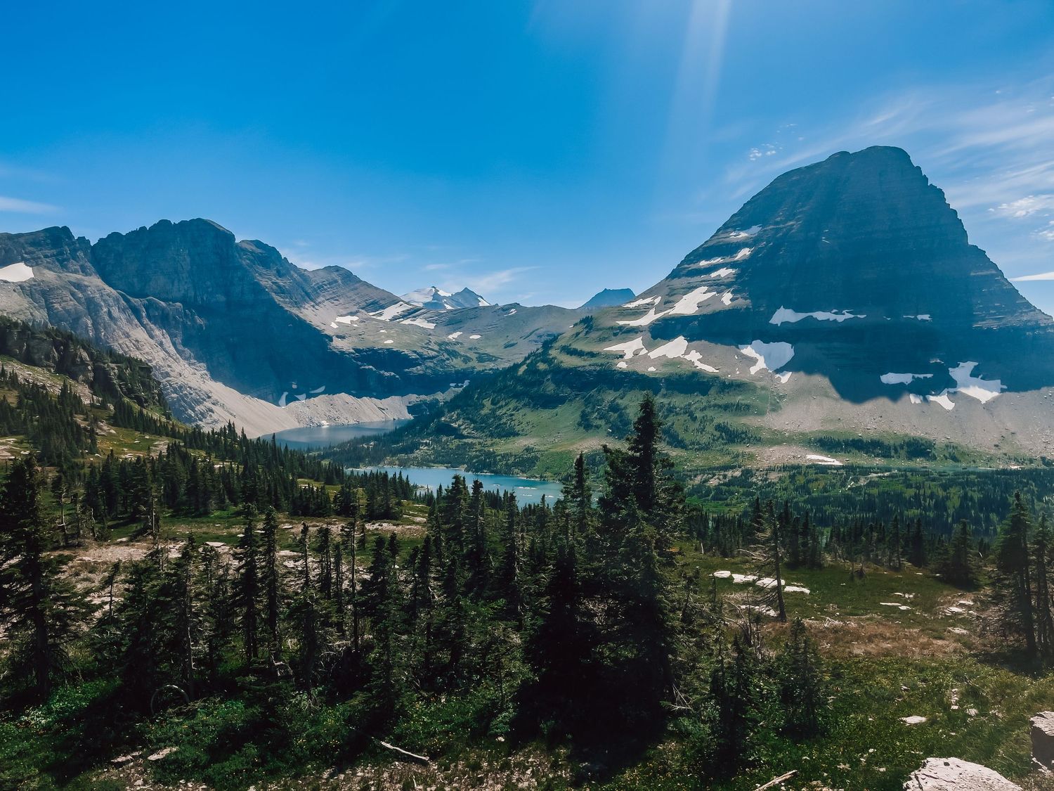 Panoramic view of snow-capped mountain peaks under bright blue summer sky.