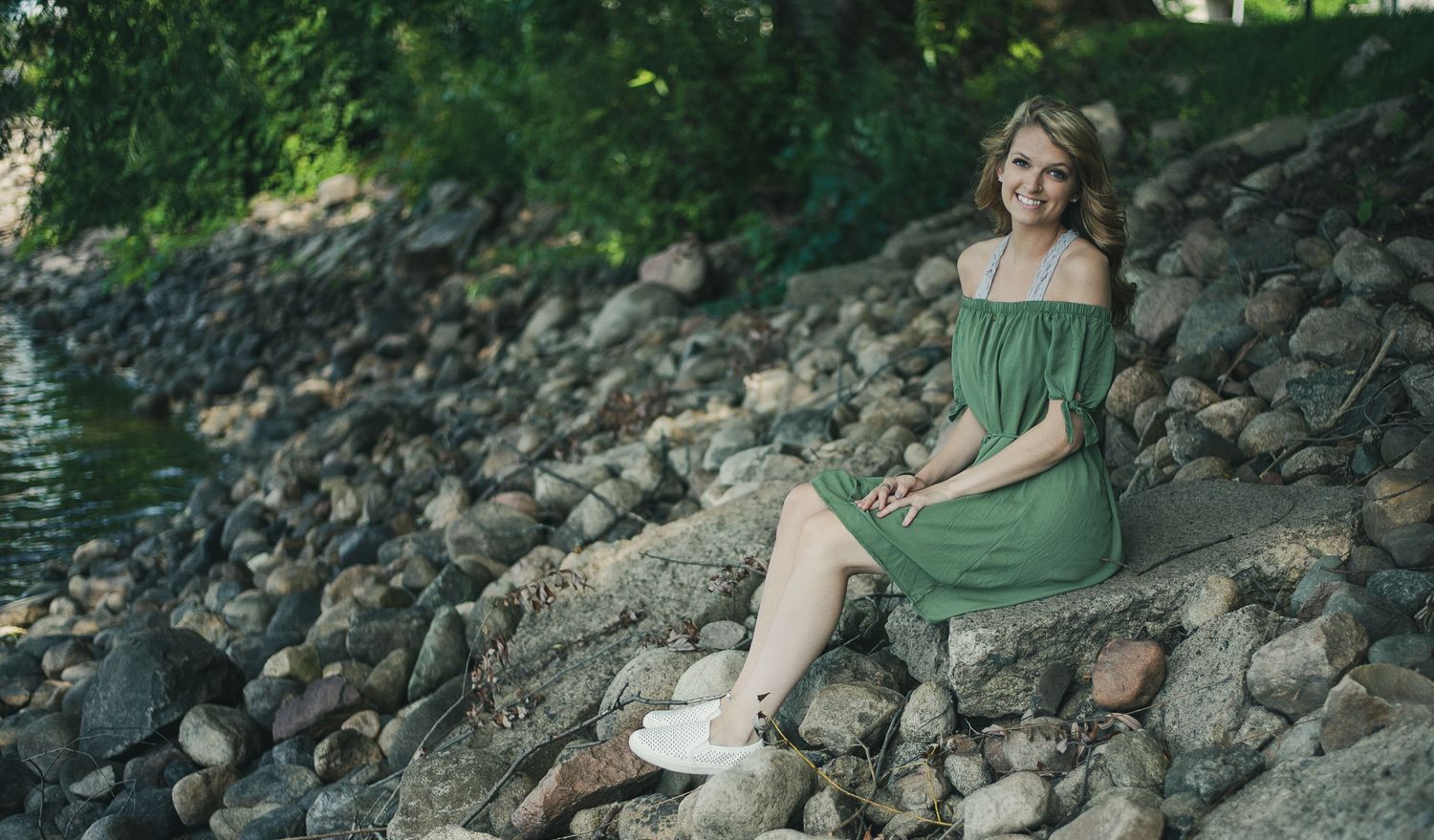 Person in green dress sitting among rocks in natural setting.