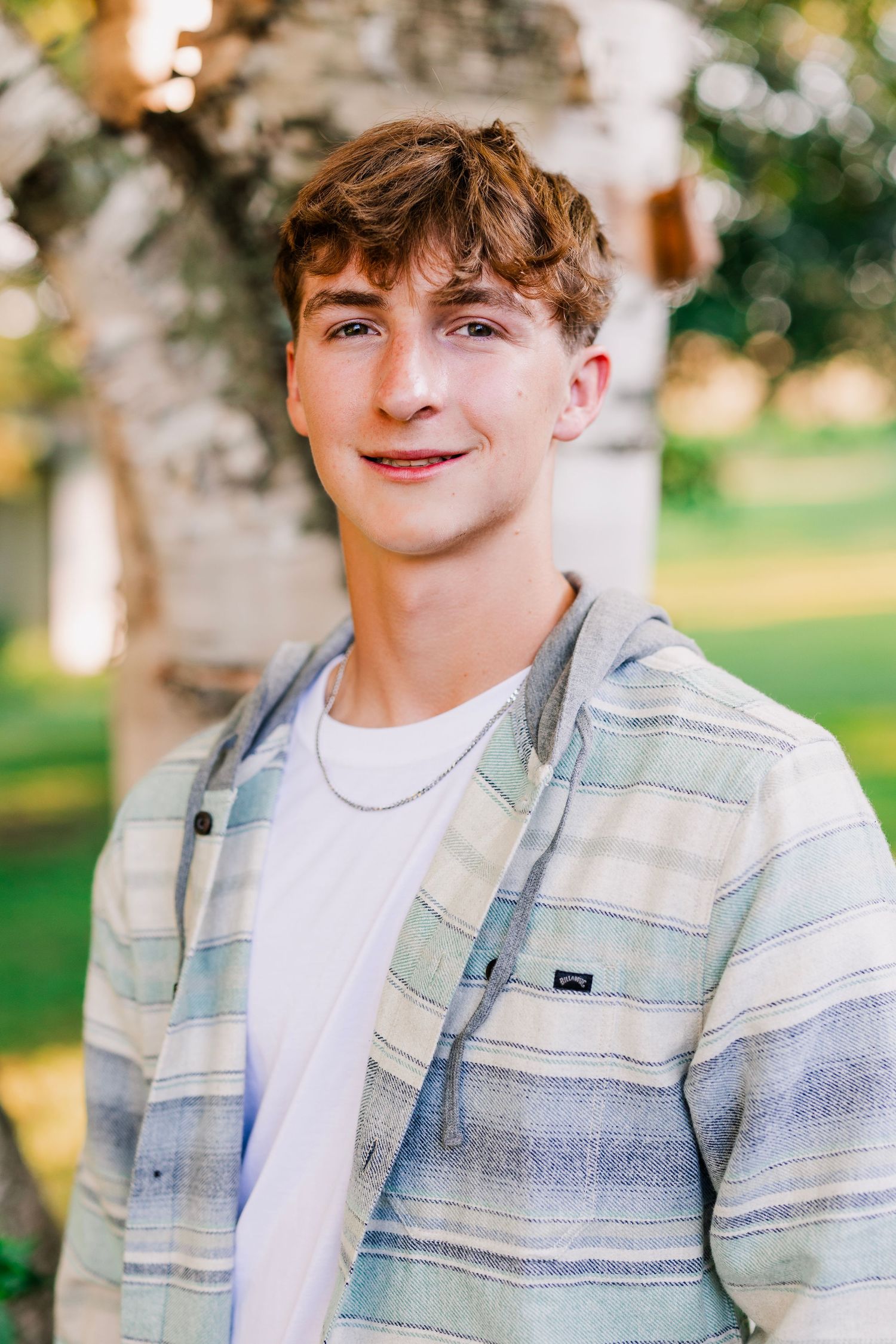 A casual portrait wearing a striped denim jacket against a natural outdoor background.