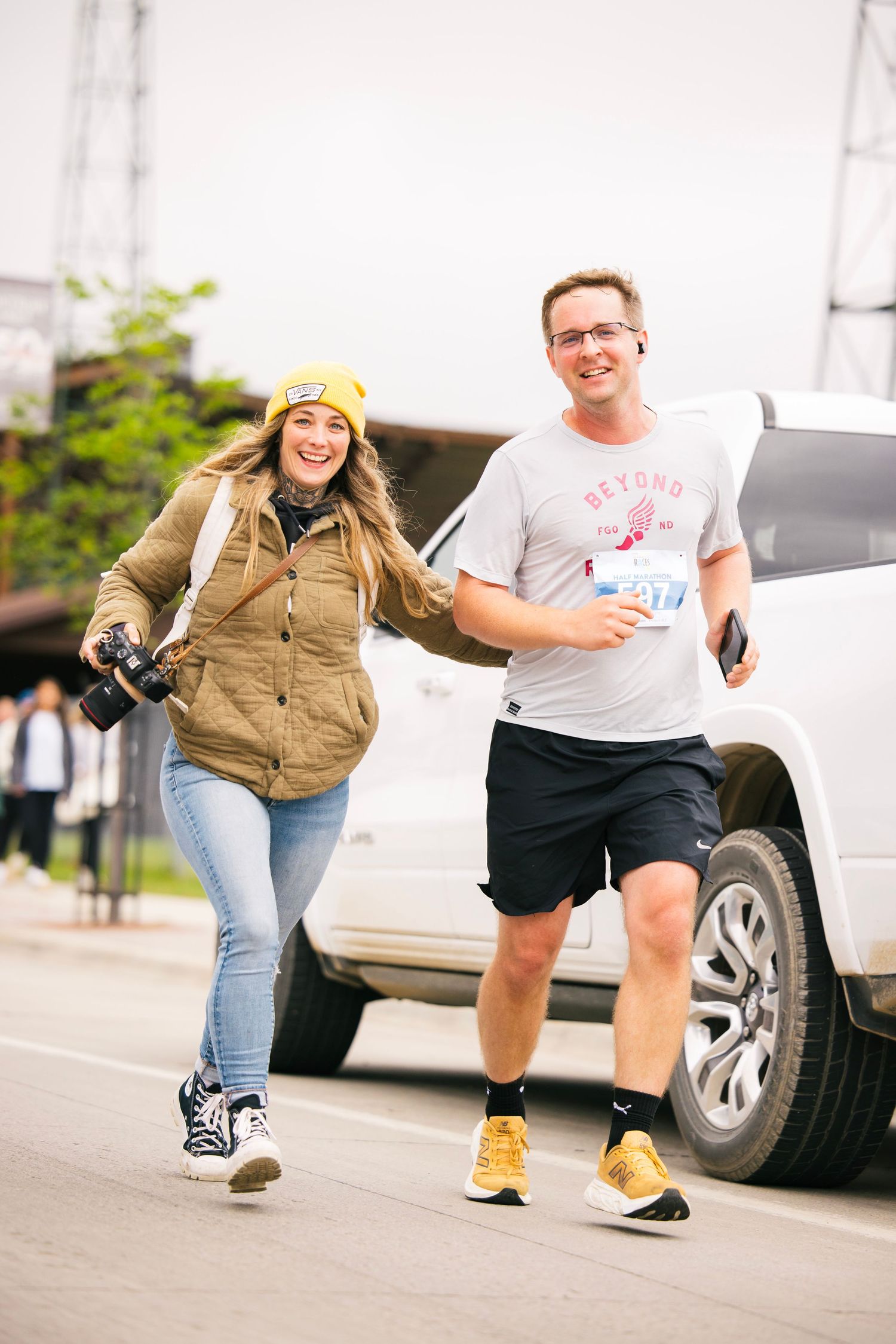 Two runners in casual attire pose playfully while racing on a suburban street.