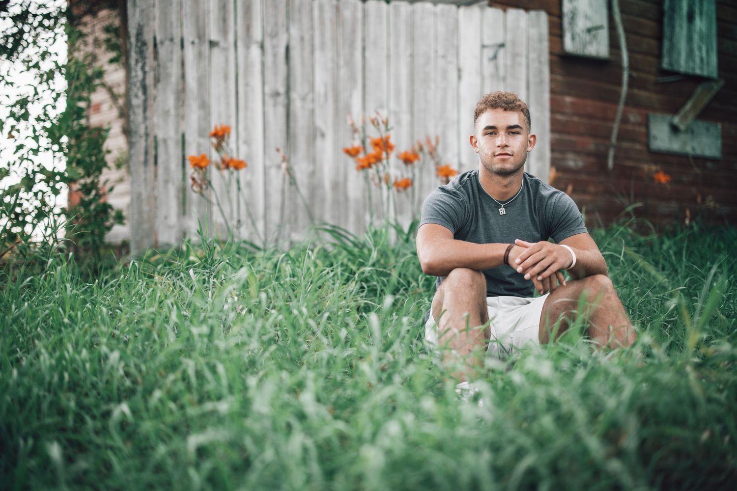Senior portraits taken against rustic wooden barn wall surrounded by greenery.