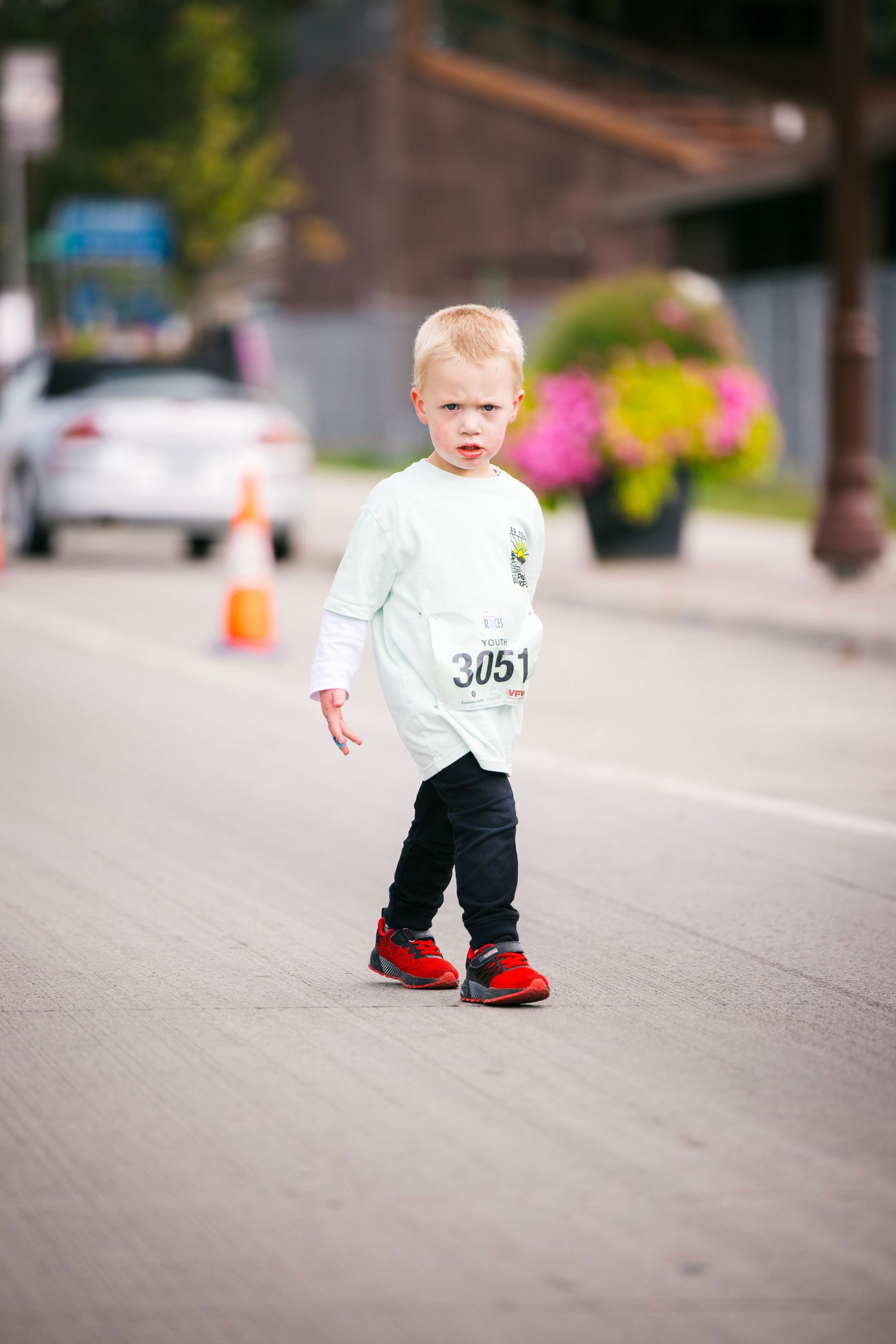 Toddler in white shirt and red shoes walking on concrete path.