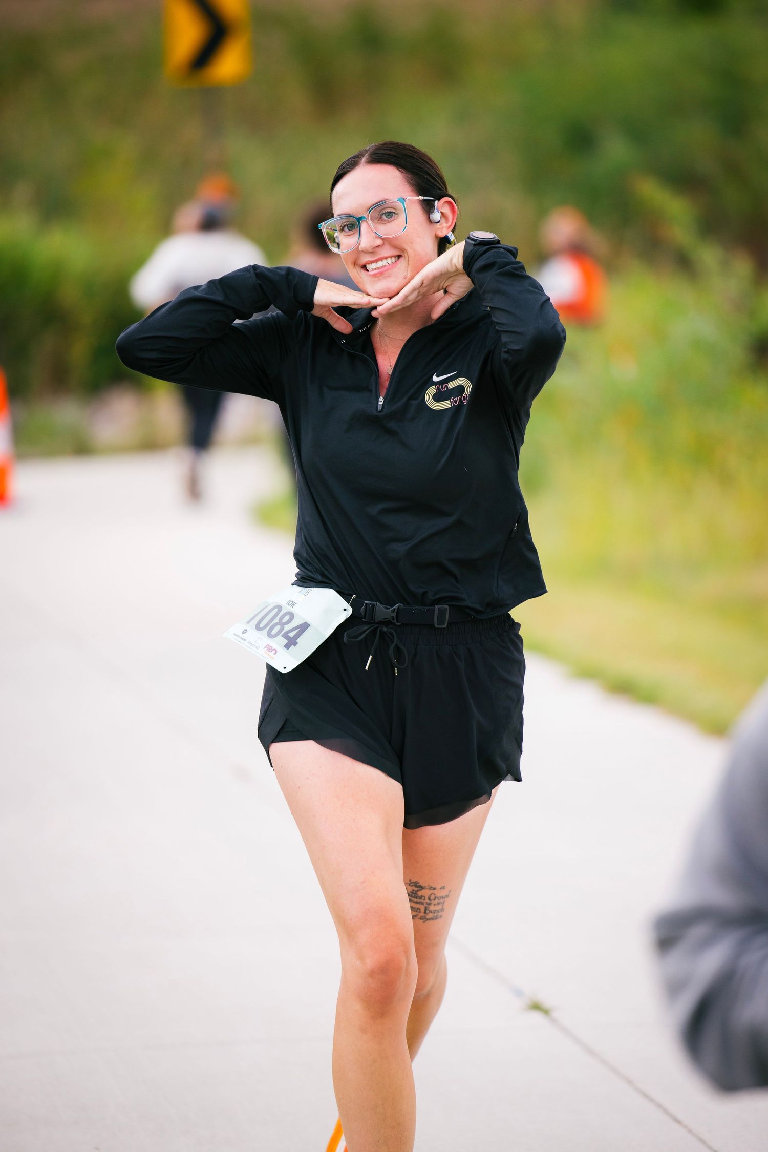 Runner in black outfit strikes playful pose during outdoor race event.