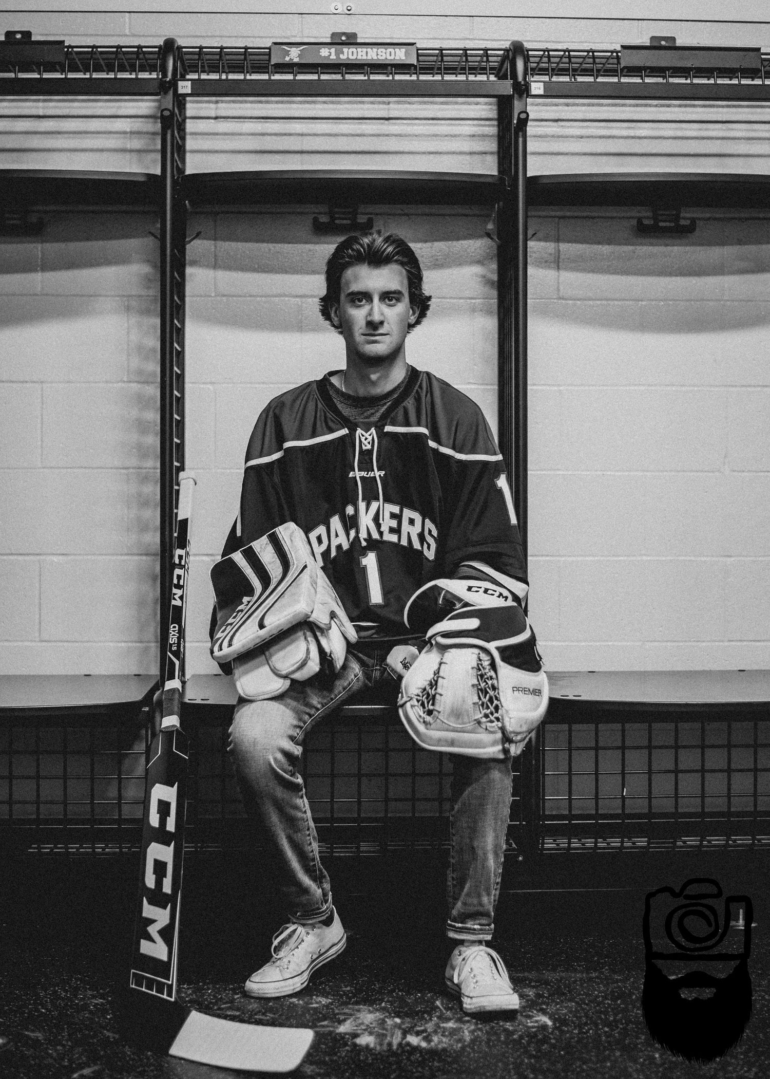 Hockey player in uniform sitting in locker room with gear and equipment.