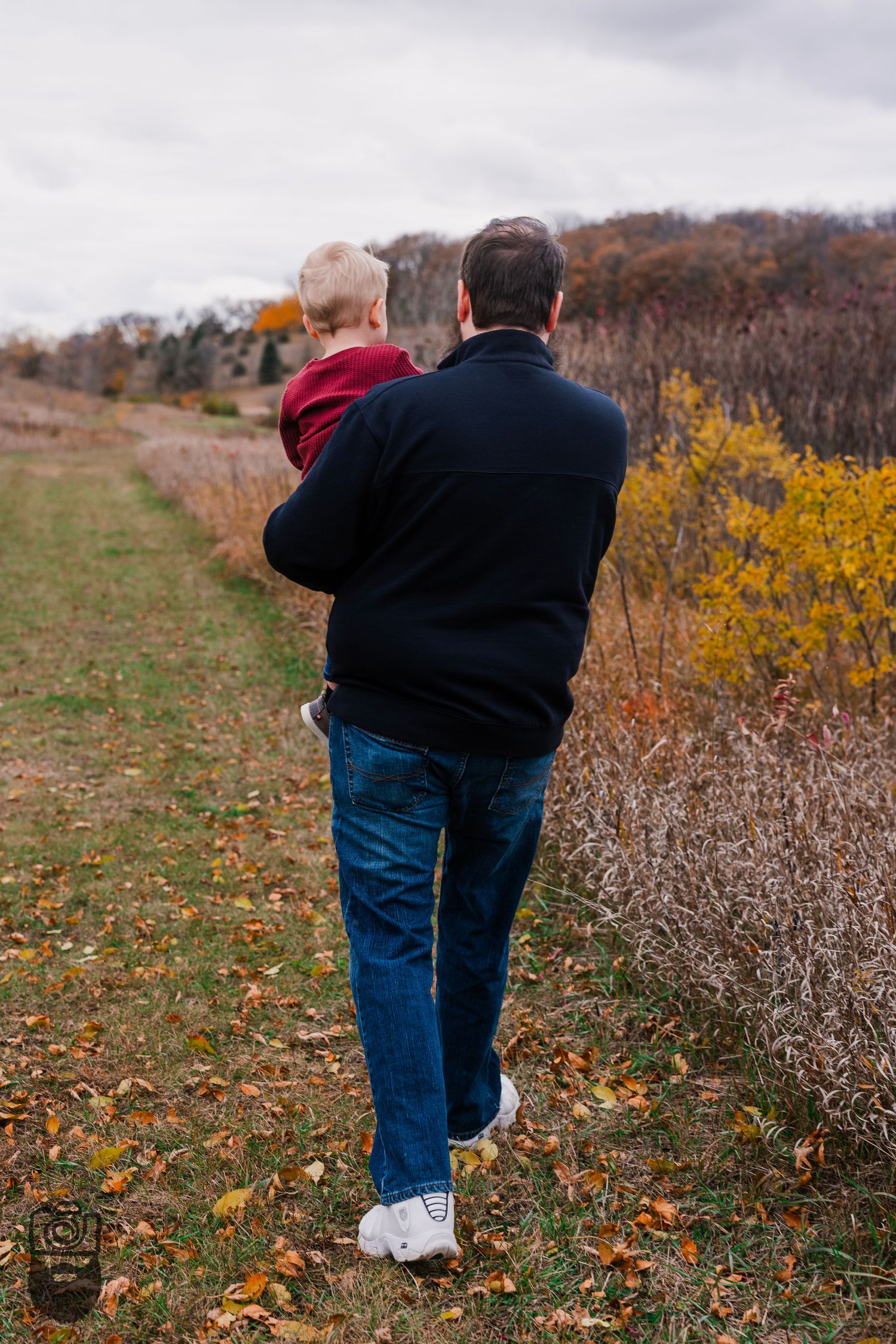People walking through autumn field with golden foliage and dried grass.