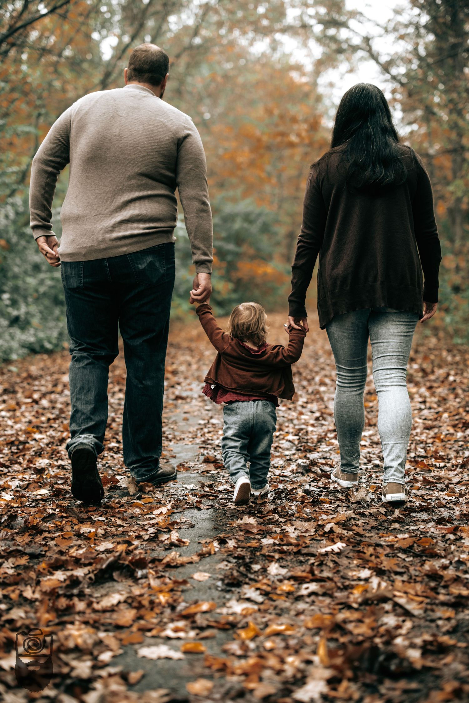 Three people walking on a path covered in fallen autumn leaves.