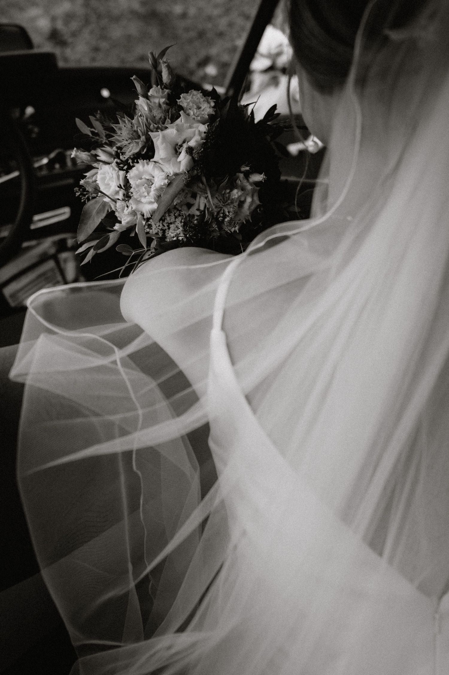 Black and white detail shot of a wedding bouquet with flowing white veil fabric.