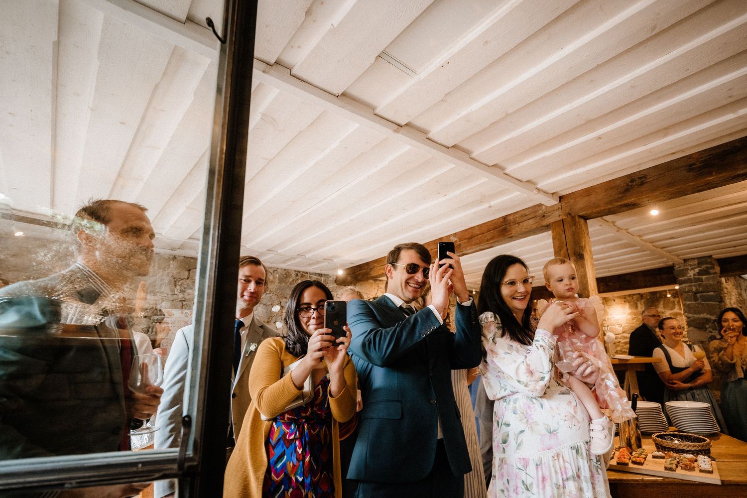 Wedding celebration with guests enjoying themselves under white beamed ceiling.