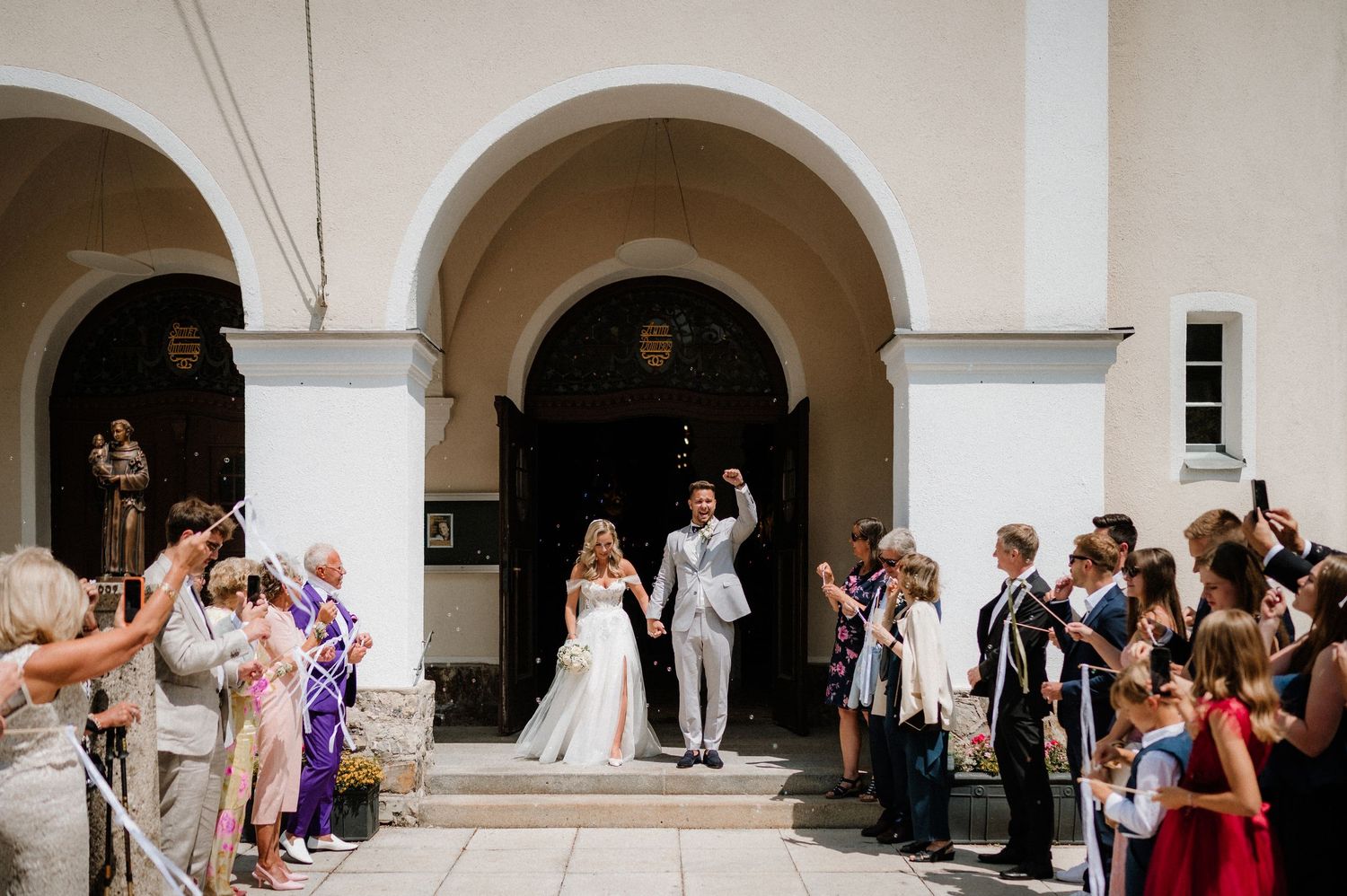 Elegant wedding celebration under white arched colonnade with guests watching the festivities.