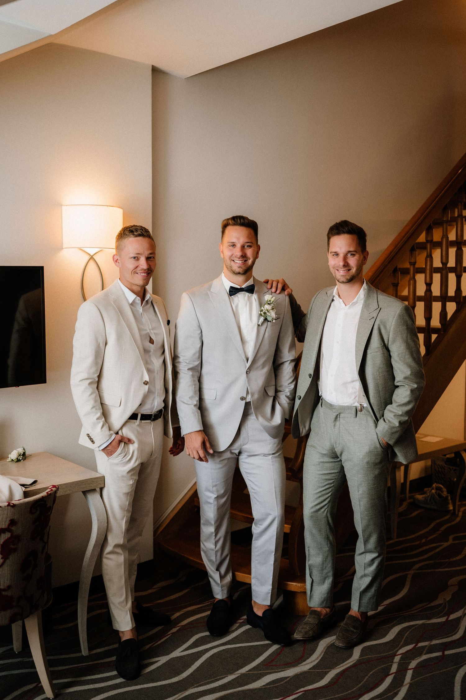 Three men in light colored suits posing together in front of a staircase.