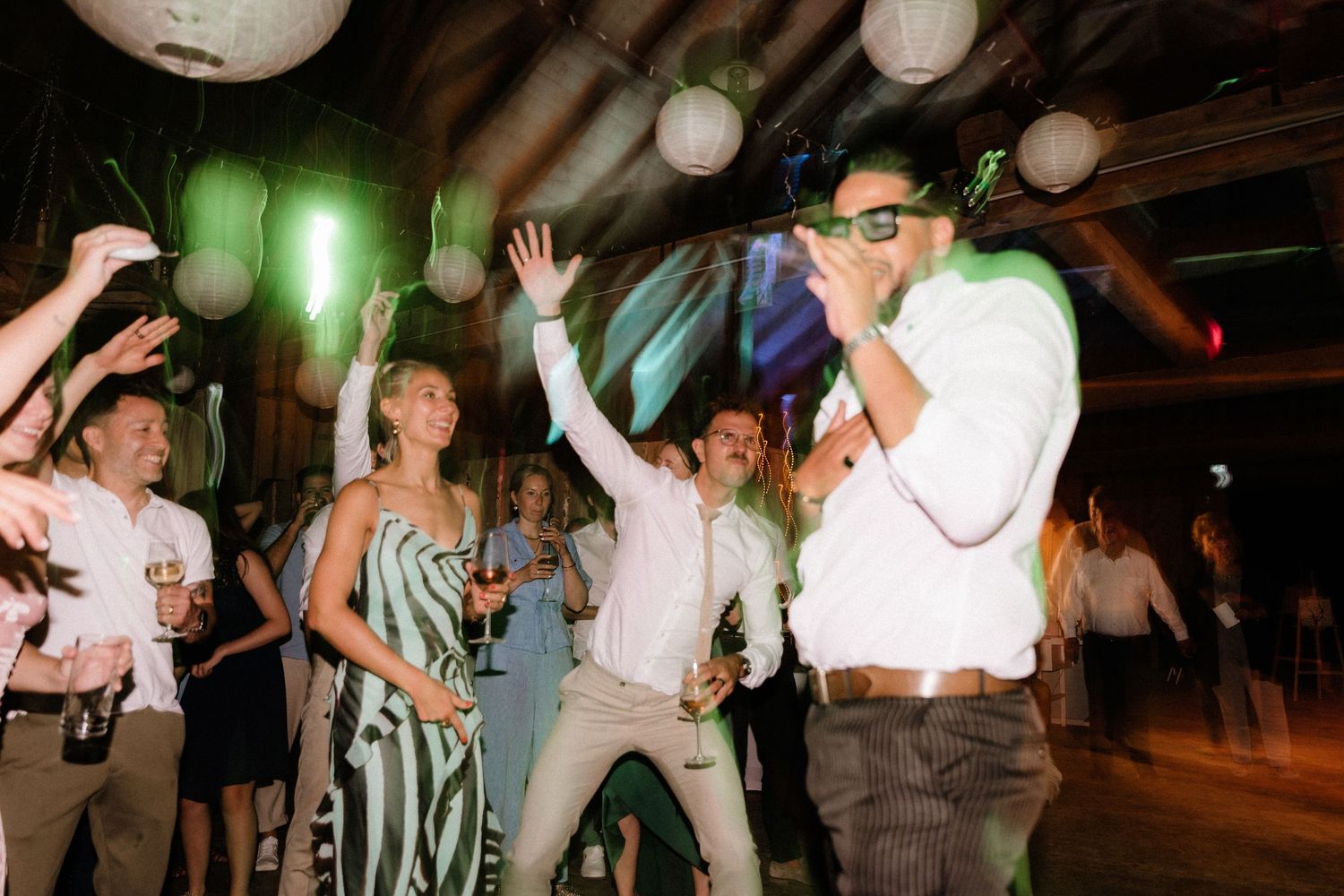 Dancers move to the music under green and white lighting at a festive indoor event.