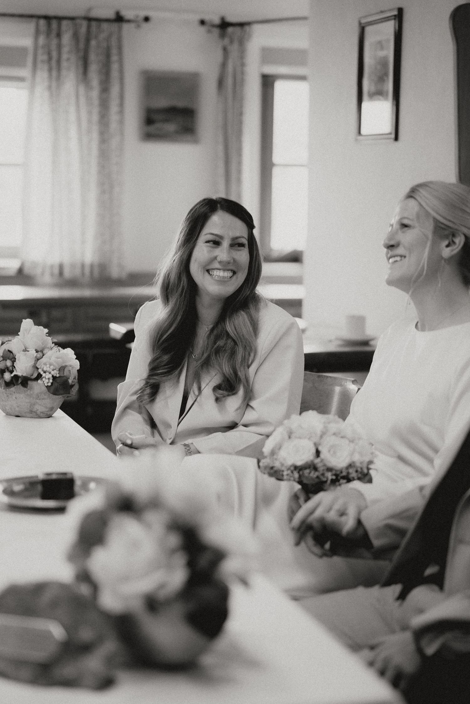 Black and white photo of wedding guests sharing candid moments at a reception table.