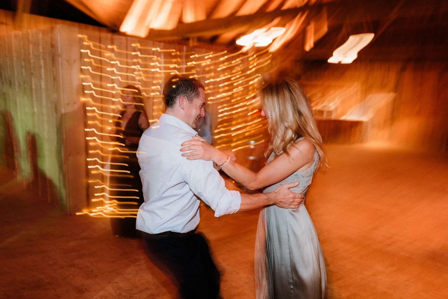 Wedding celebration with warm orange lighting and string lights creating an intimate dance floor atmosphere.