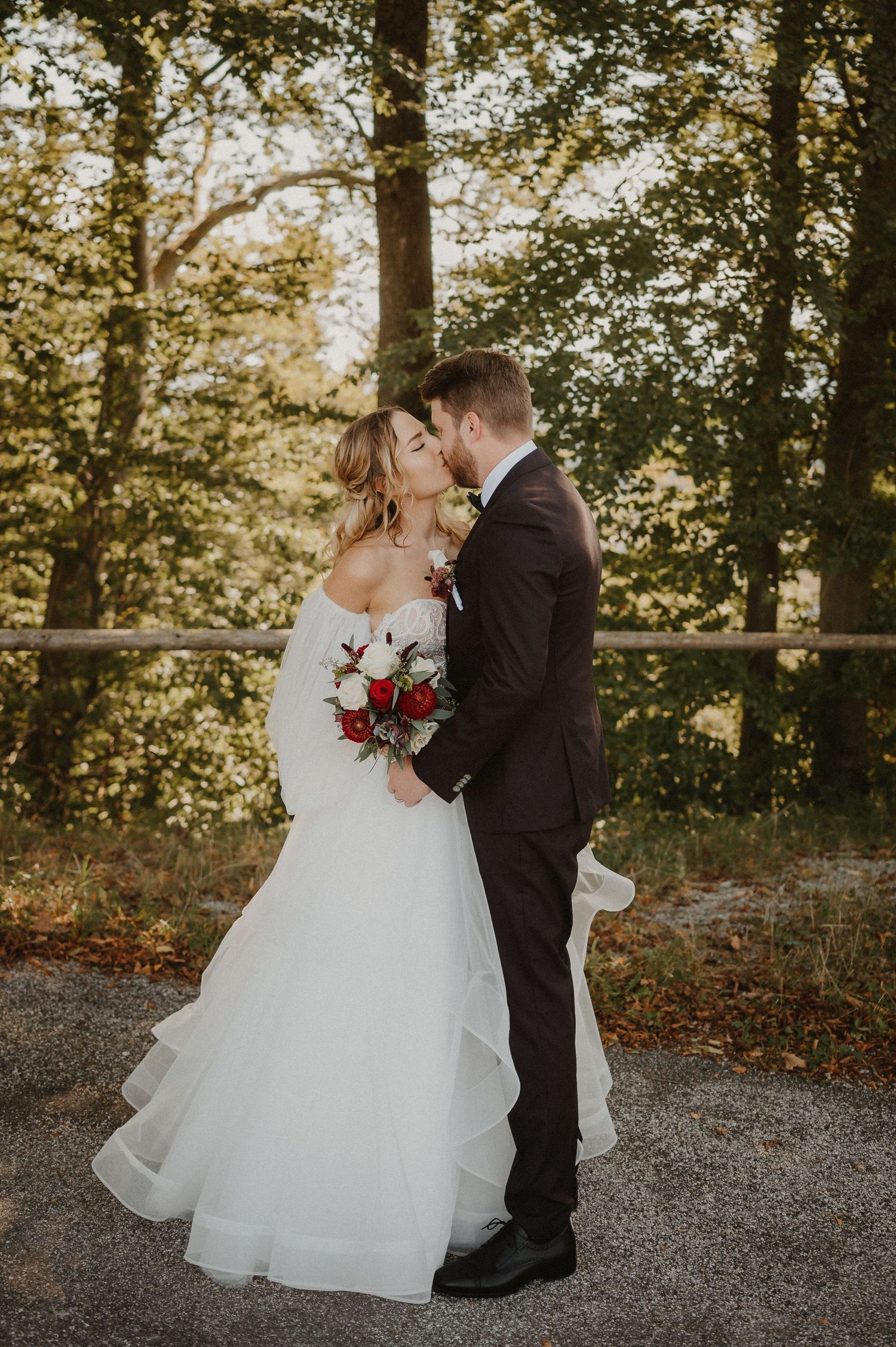 Romantic autumn wedding portraits on gravel path surrounded by golden trees.