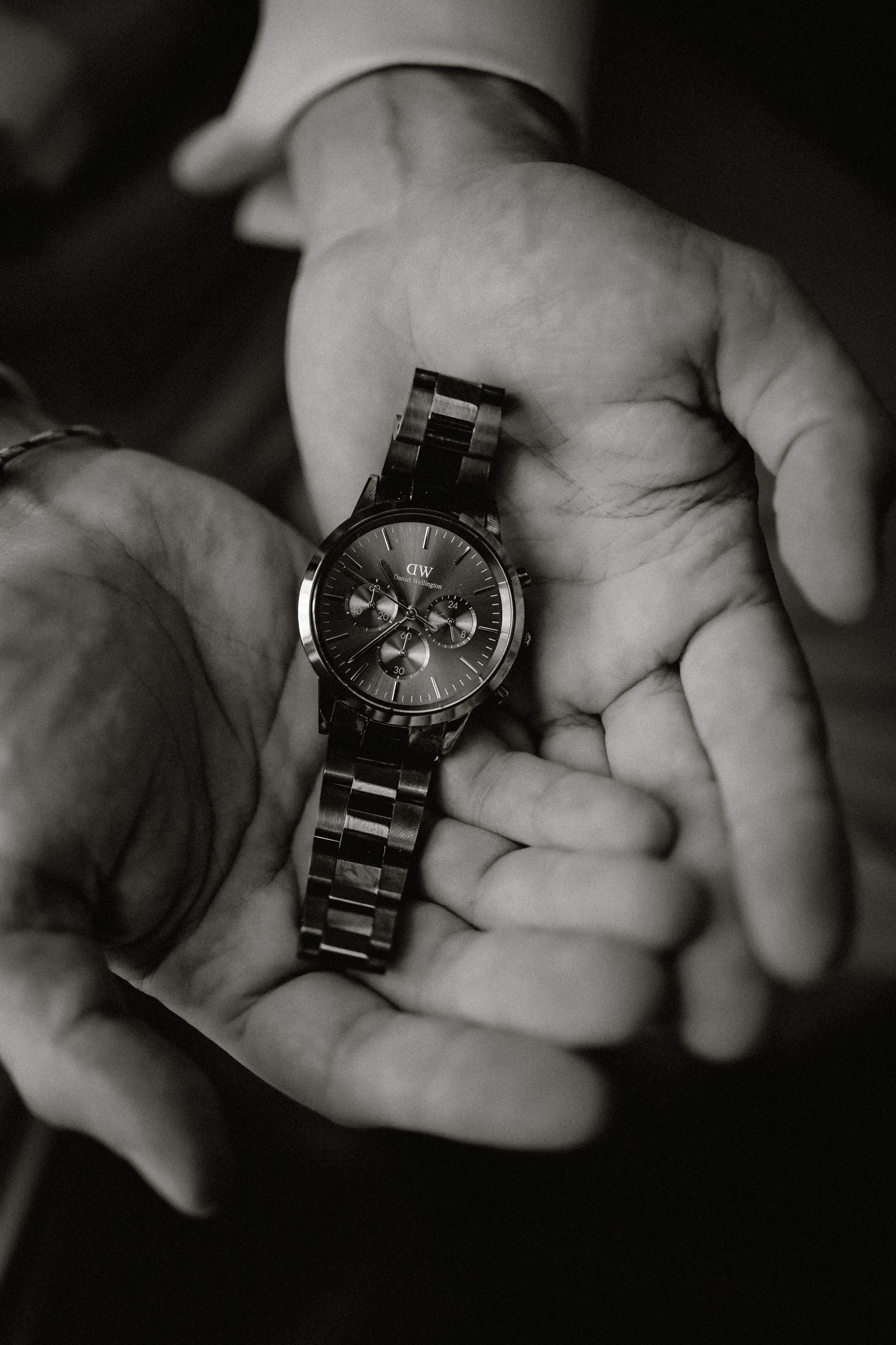 Black and white close-up of hands holding a metal chronograph watch.