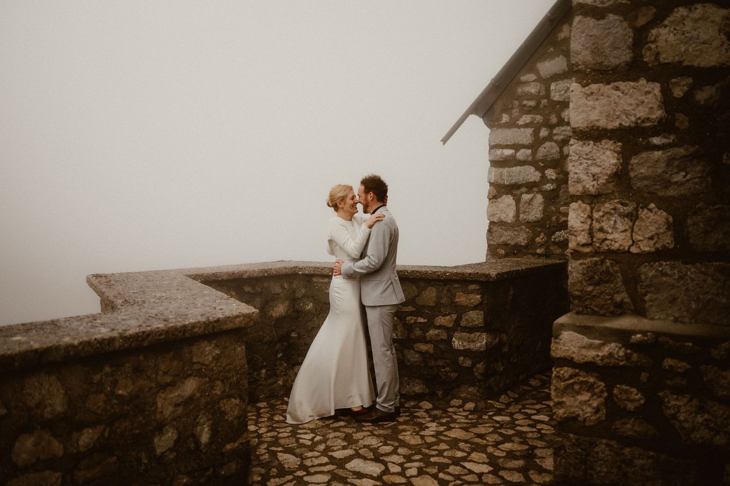 Intimate wedding portrait on a cobblestone terrace surrounded by mountain mist.