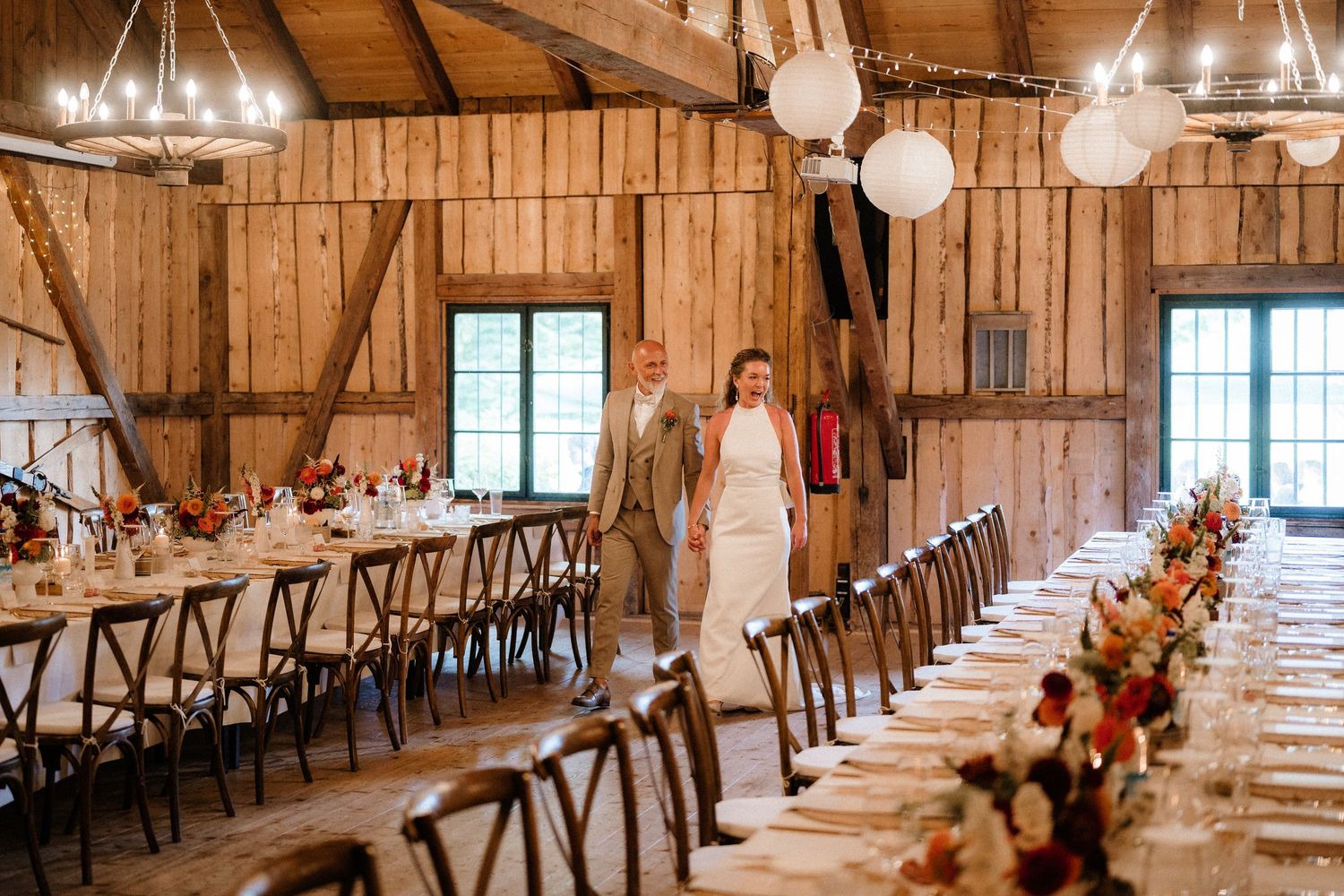 Interior of a barn wedding venue with elegant table settings and hanging lanterns.