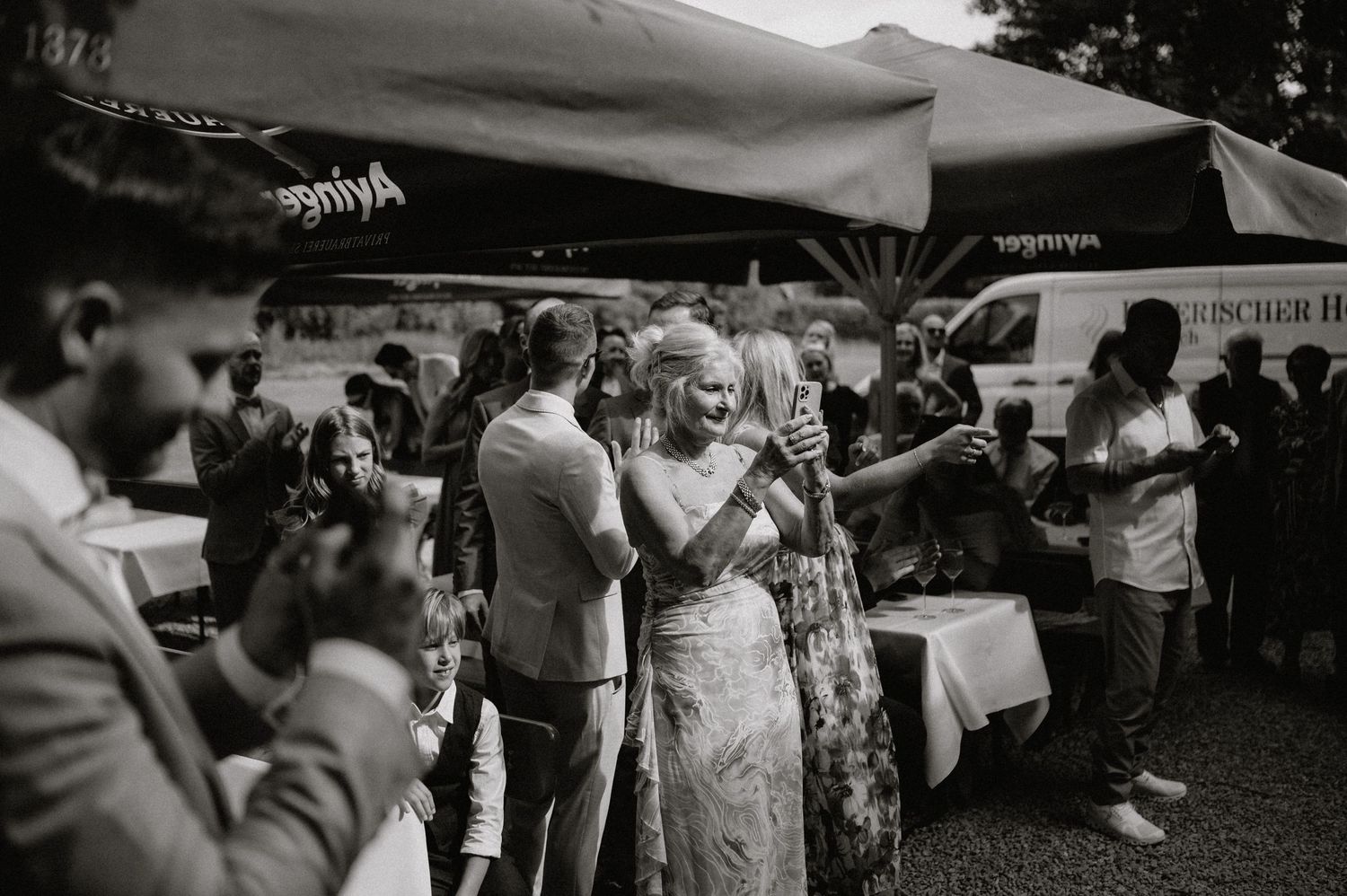 Wedding guests gather outdoors under a tent during a sunny celebration.