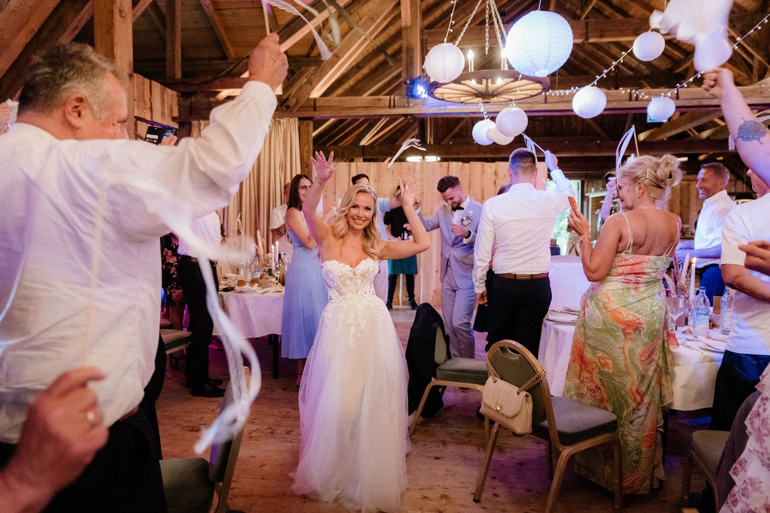 Wedding reception dance party in rustic barn with purple lighting and paper lanterns.